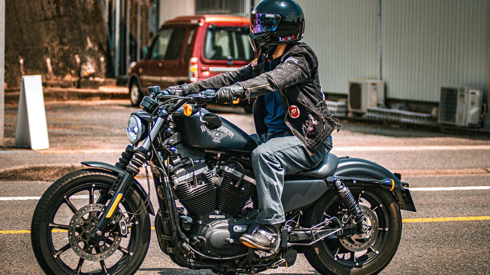 A biker in helmet rides a Harley Davidson motorcycle on a city street during the day.