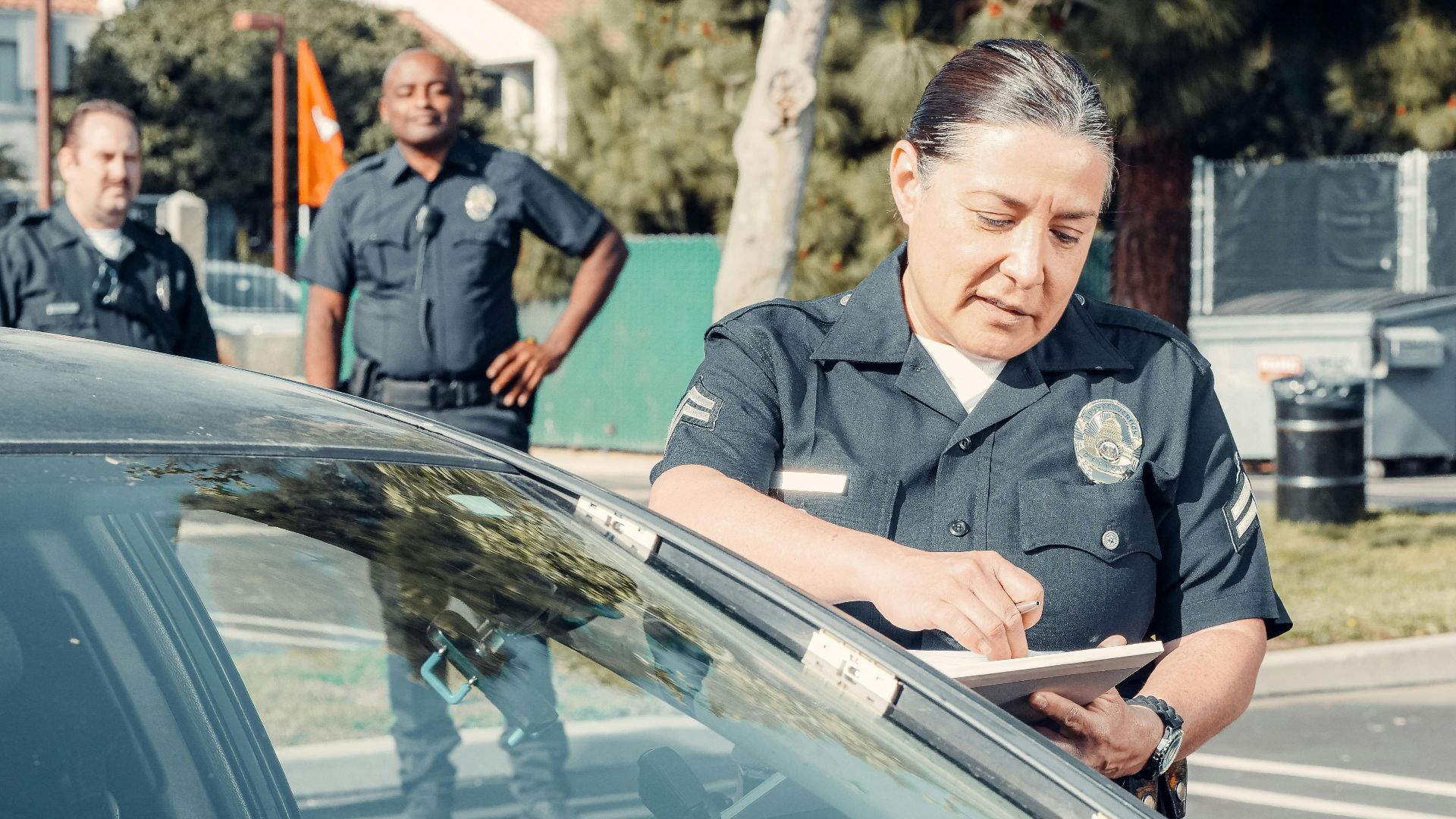 Police officers handling a traffic violation in a parking lot, focus on policewoman writing a ticket.
