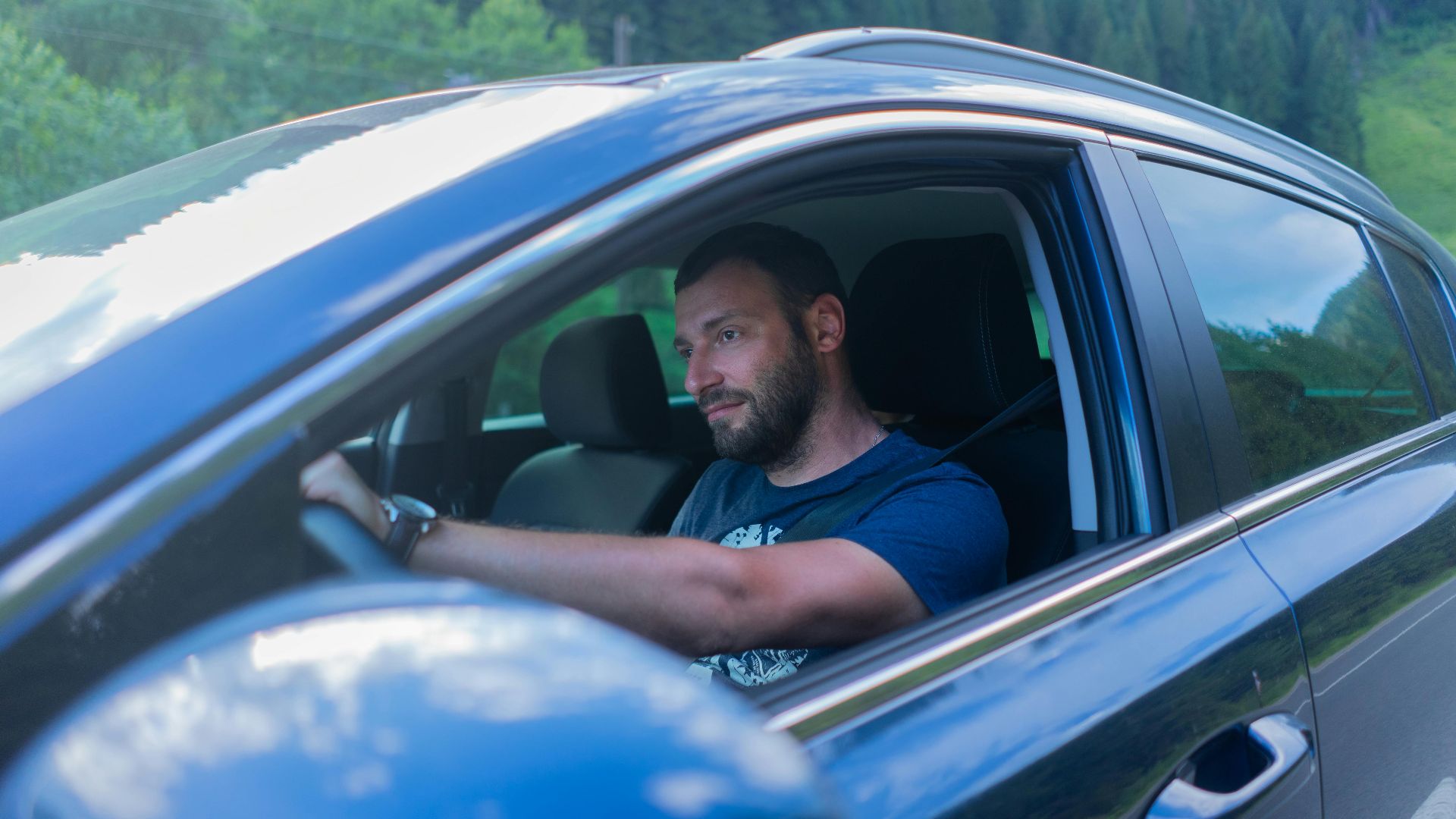 Bearded man enjoying a drive through lush green countryside on a sunny day.