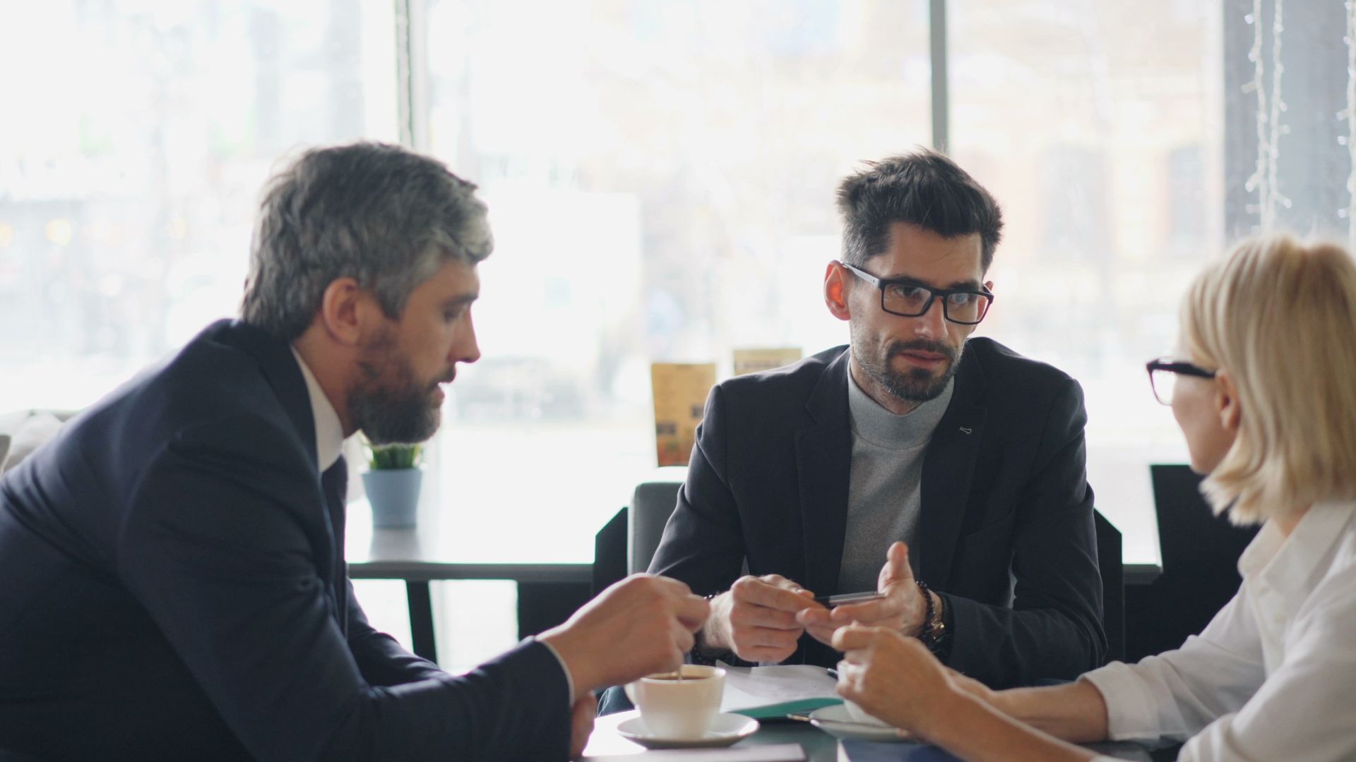 Three professionals engaging in a business discussion over coffee in a modern café setting.