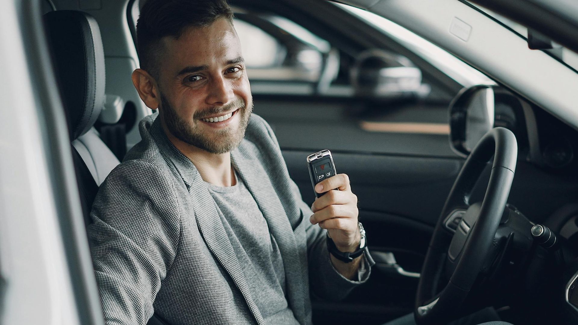 Happy man holding car keys while seated inside a modern vehicle.