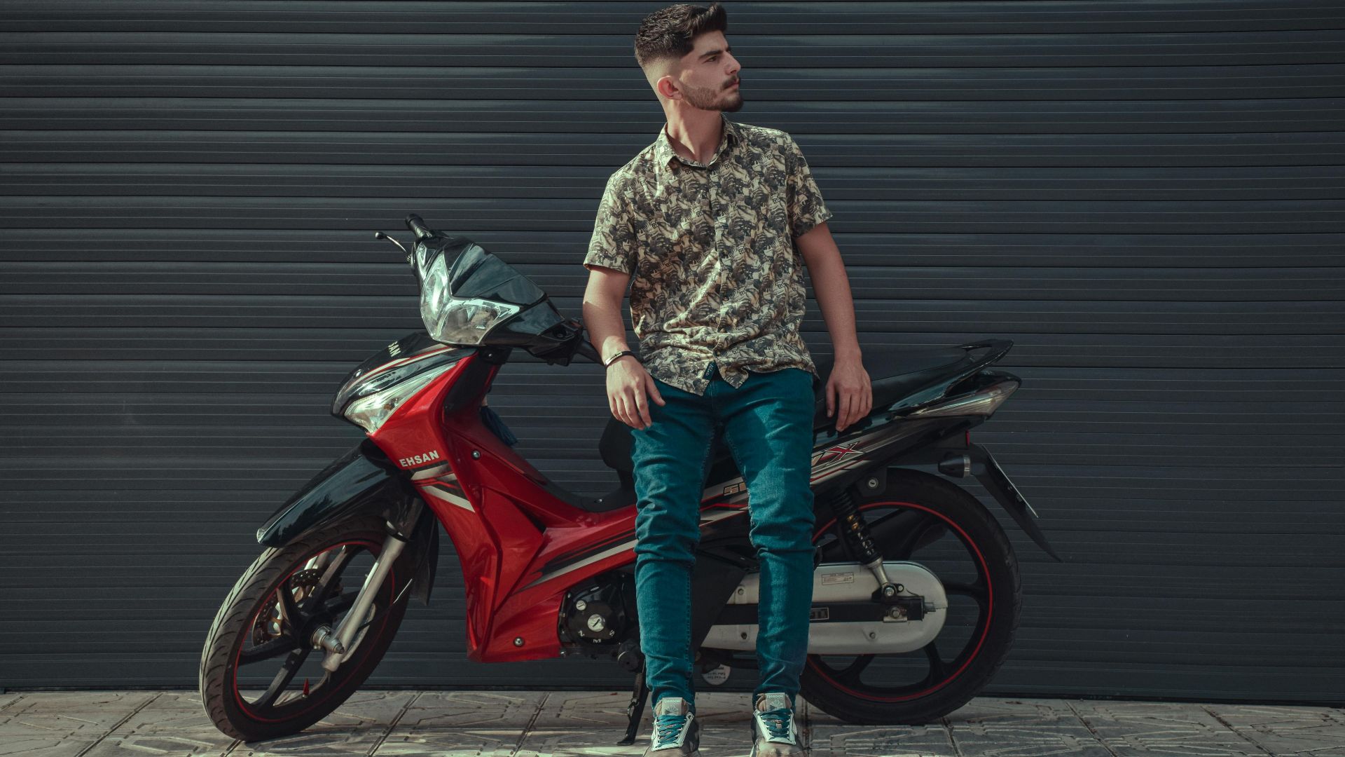 Stylish man leaning on a red motorcycle with urban background.