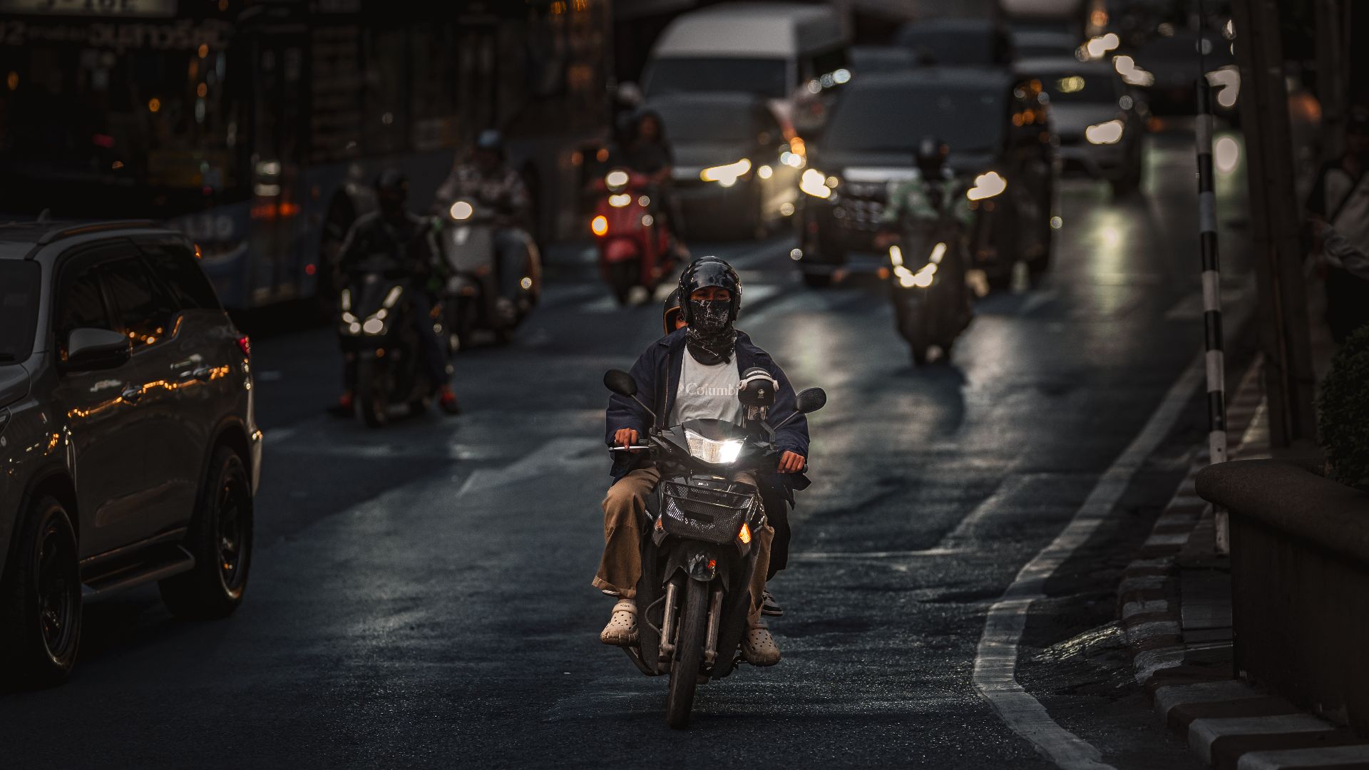 A motorcyclist navigates through busy evening traffic in Bangkok, Thailand.