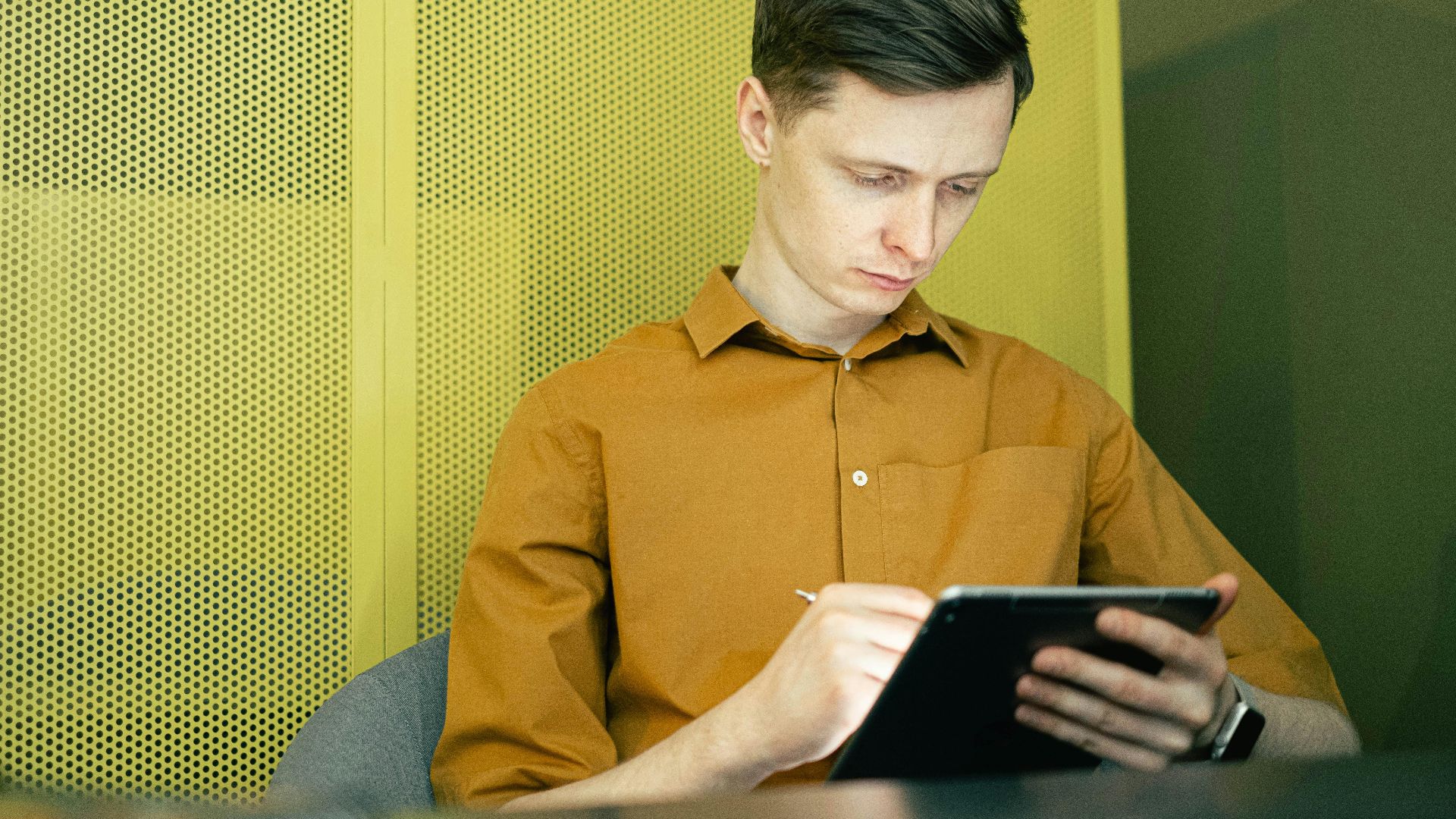Young man in yellow shirt focused on using a tablet indoors, showcasing modern technology and study.