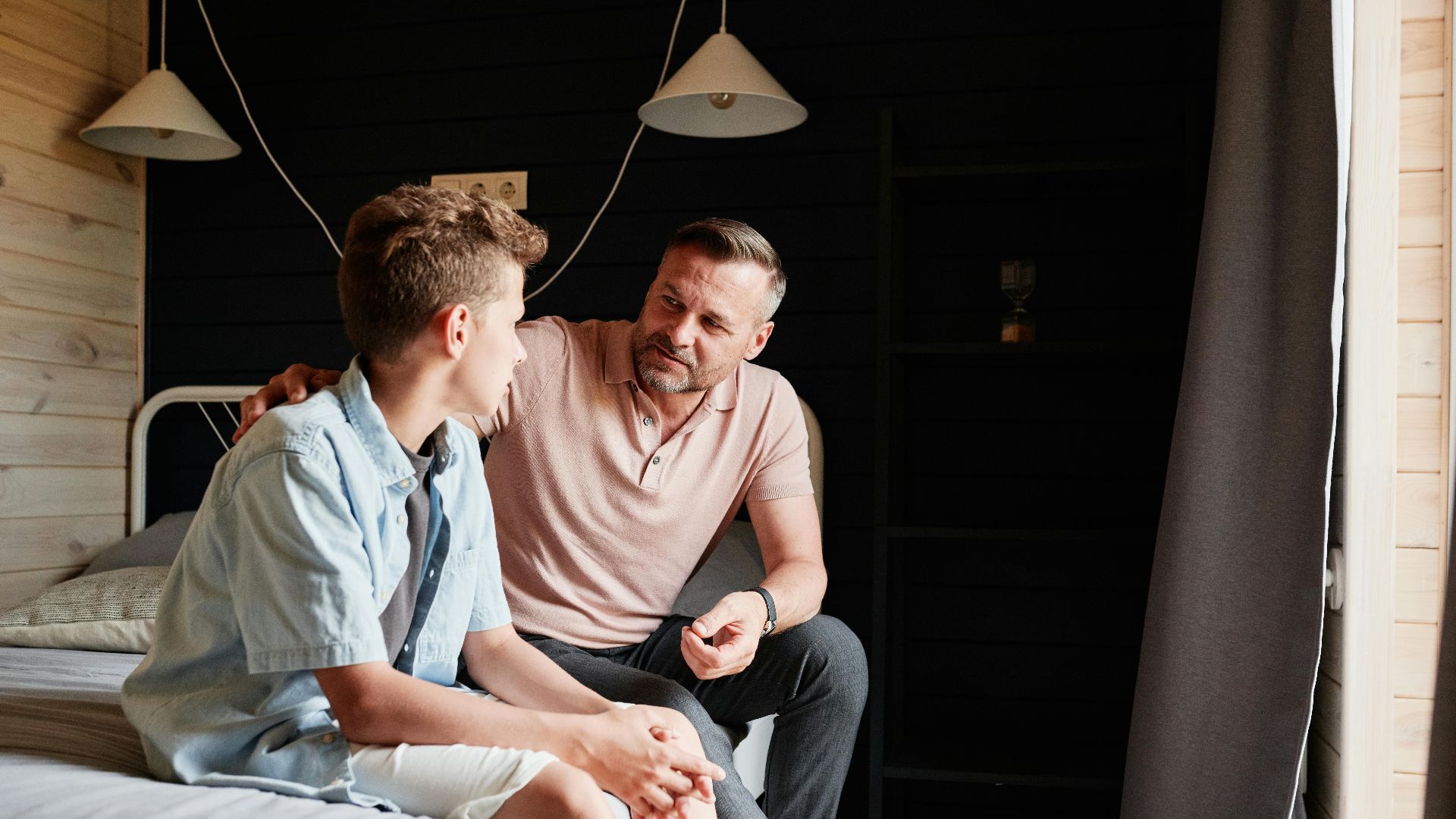 A father bonding with his teenage son in a cozy bedroom, sharing advice and conversation.