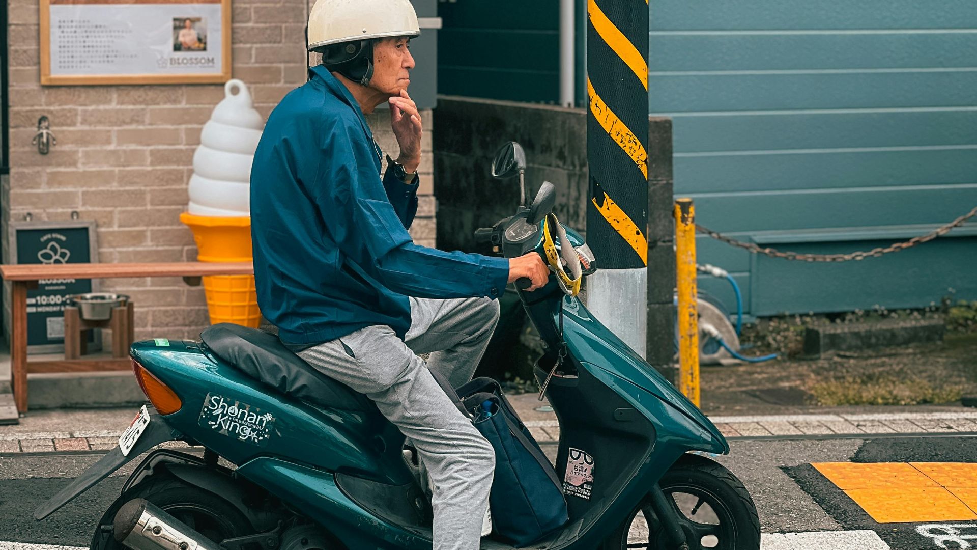 A man wearing a helmet sits on a scooter at a city intersection. Urban lifestyle scene.