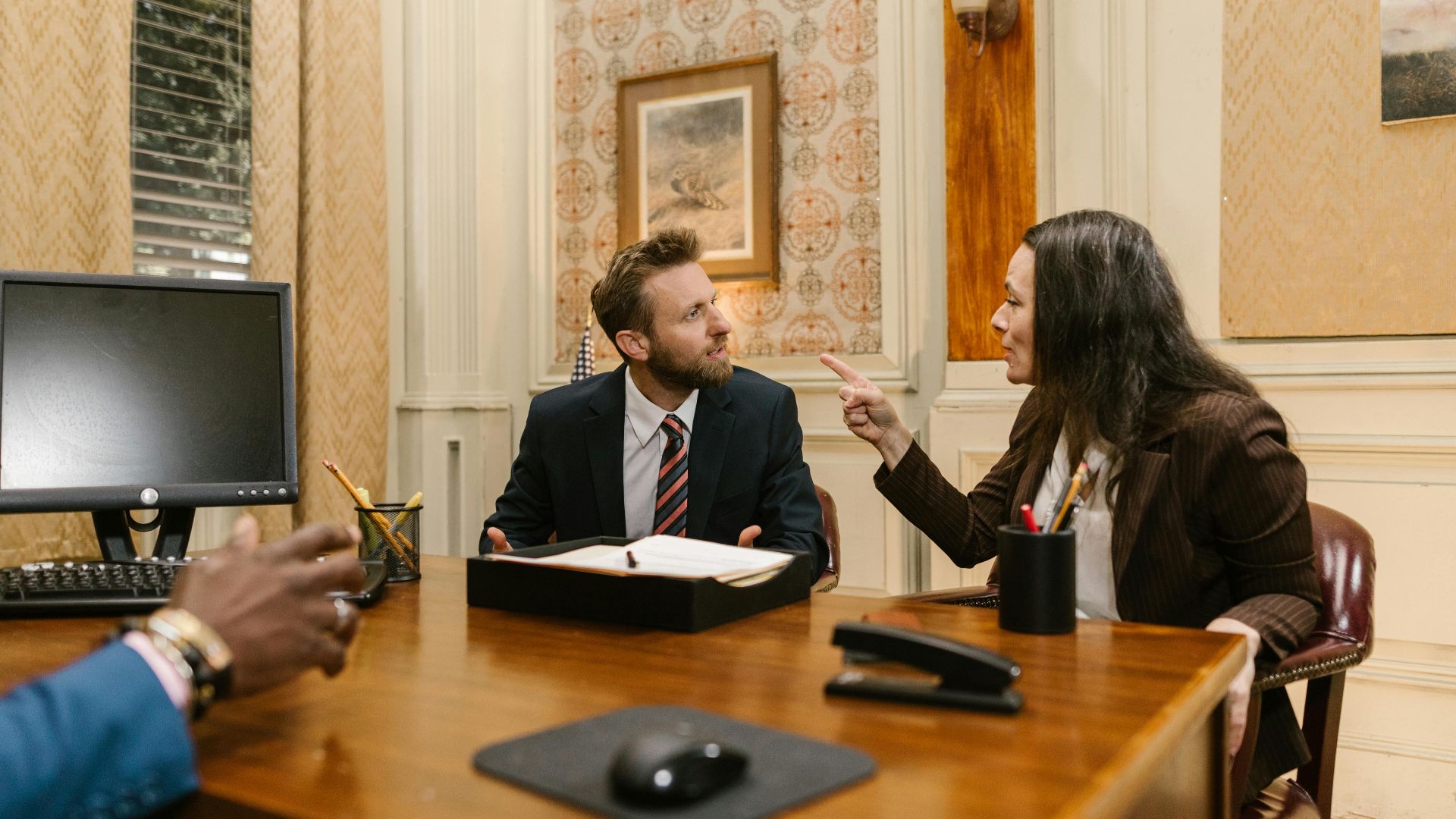 Professionals engaged in a serious discussion inside a law office with a computer on the desk.