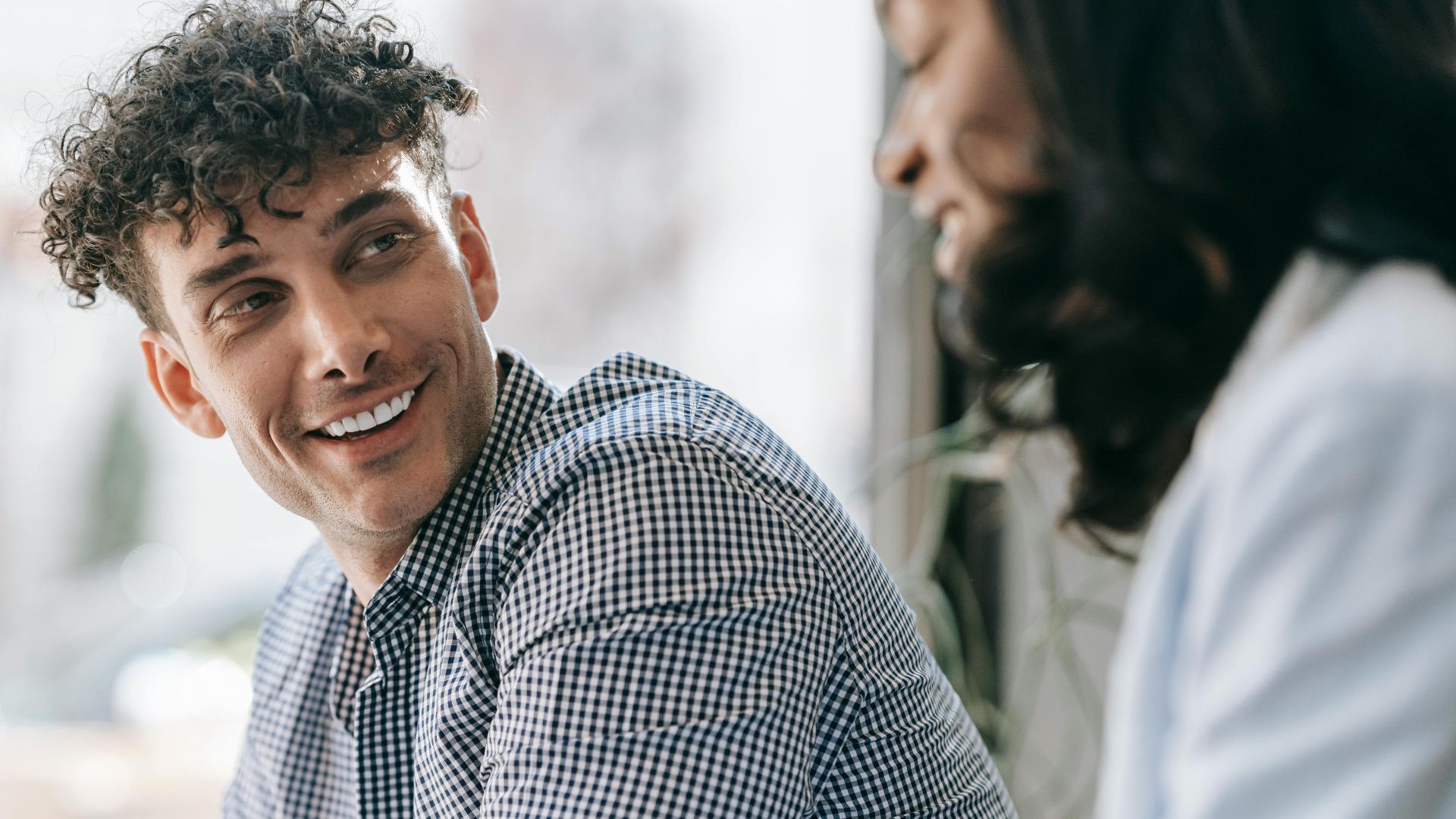 Caucasian man and black woman sharing a friendly smile indoors with natural light.