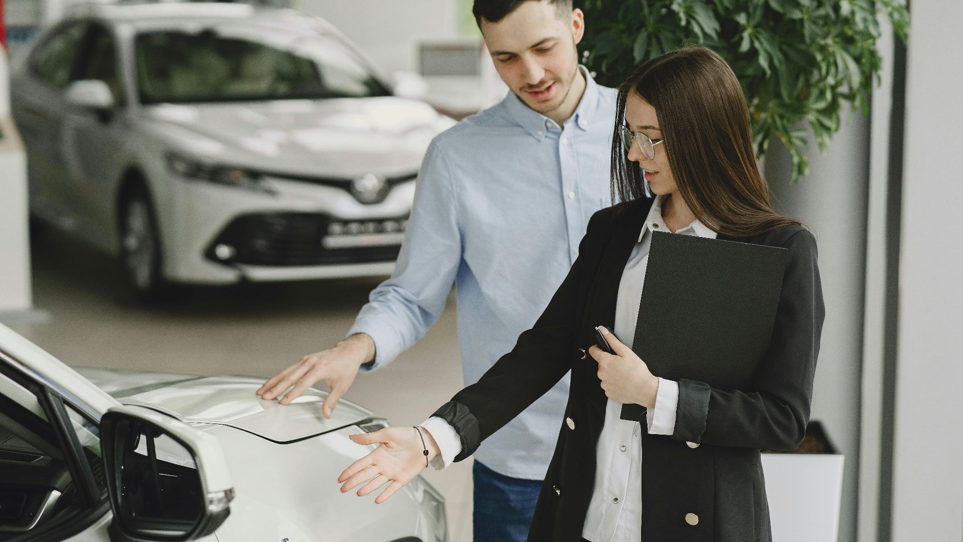 A man and saleswoman discussing a hybrid vehicle's features in an indoor showroom.