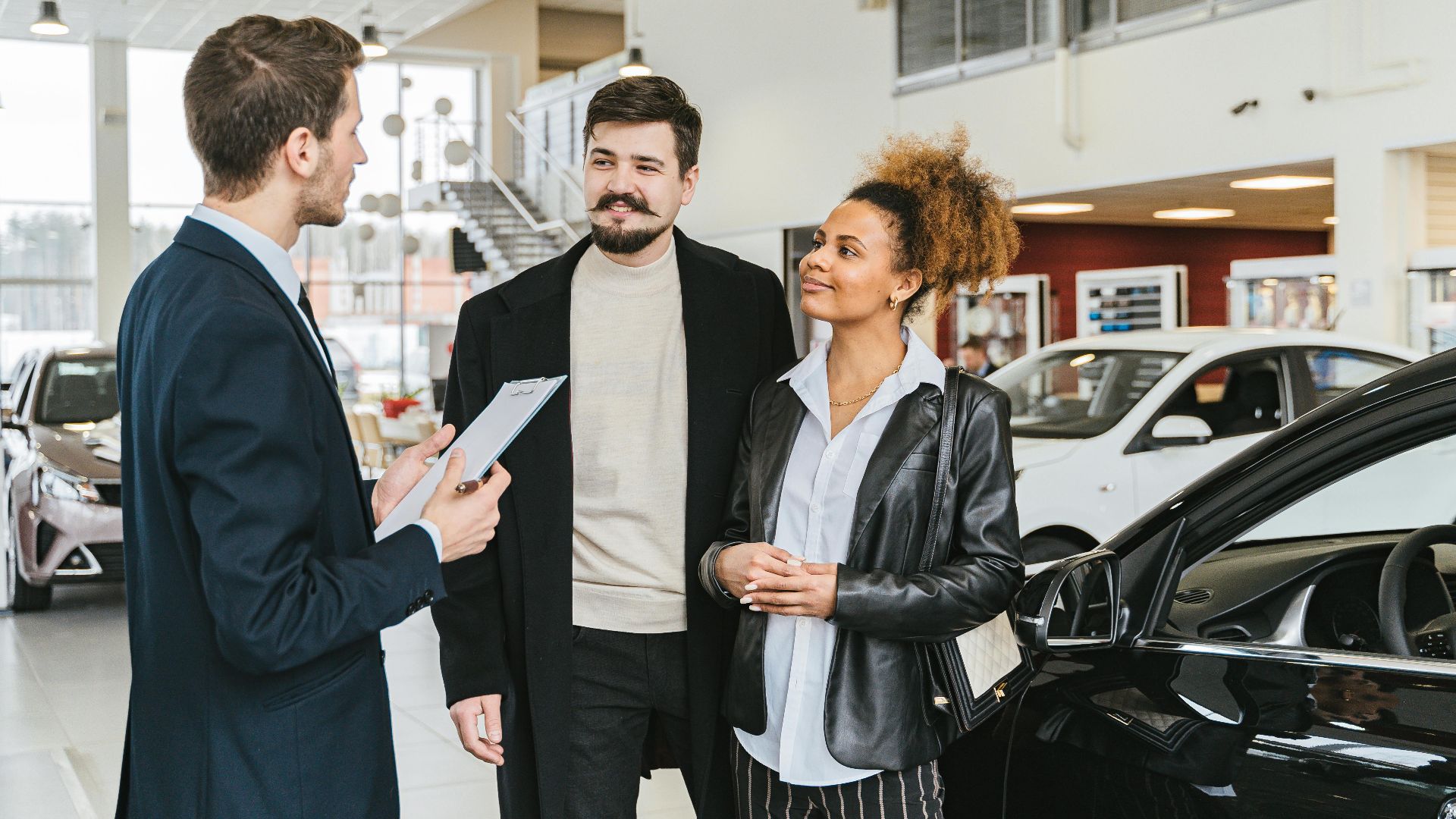 Couple discussing car purchase with salesman at indoor dealership, engaging conversation.