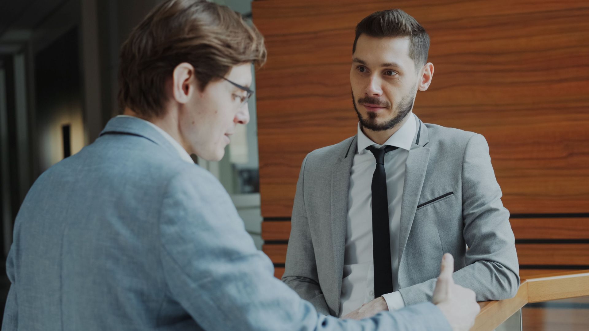 Two male professionals engaged in conversation in a modern office setting.