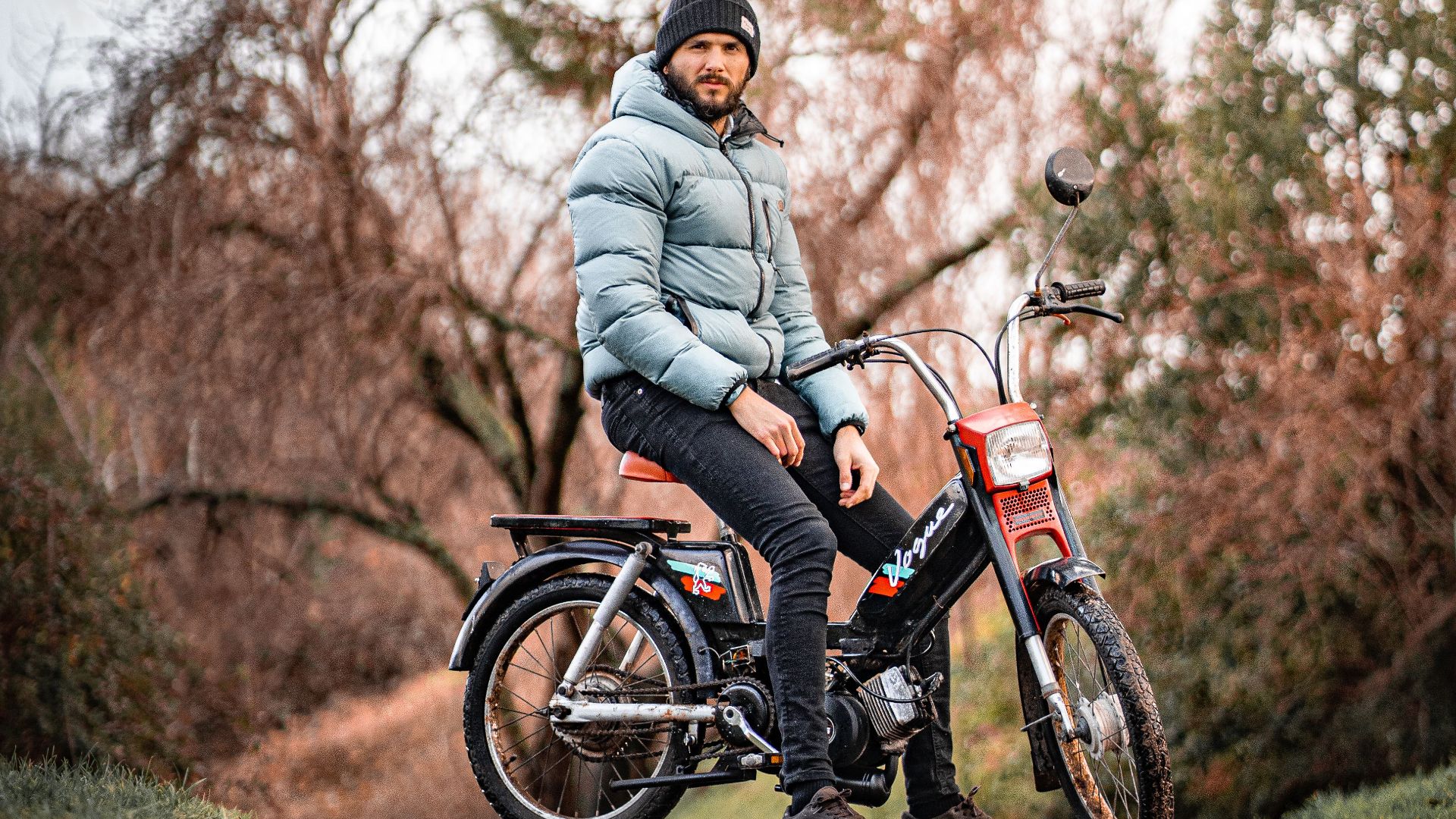 A man enjoys a leisurely ride on a vintage motorcycle through a forest trail in fall.
