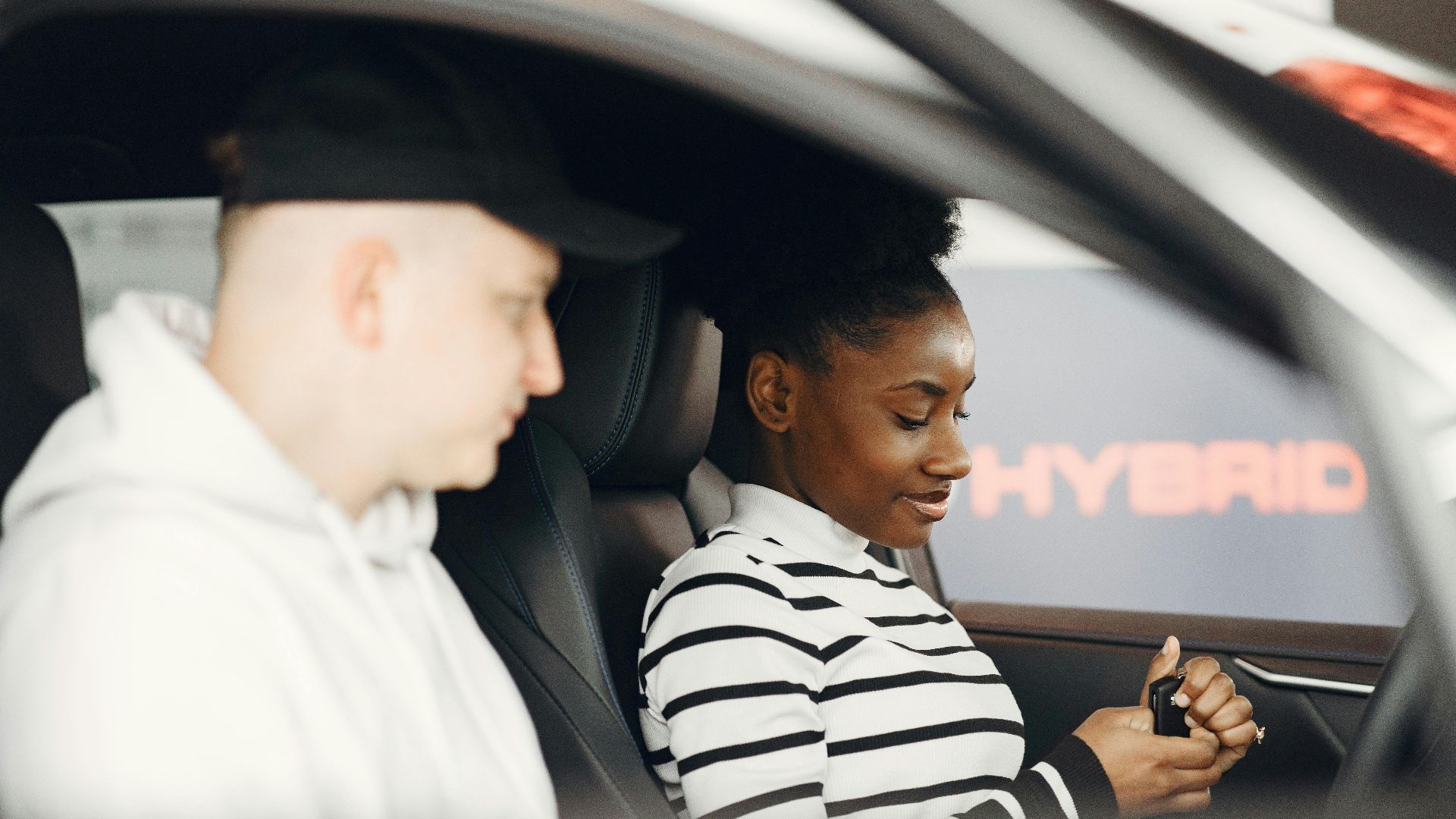 A man and woman sitting inside a hybrid car, discussing its features, highlighting modern eco-friendly transportation.