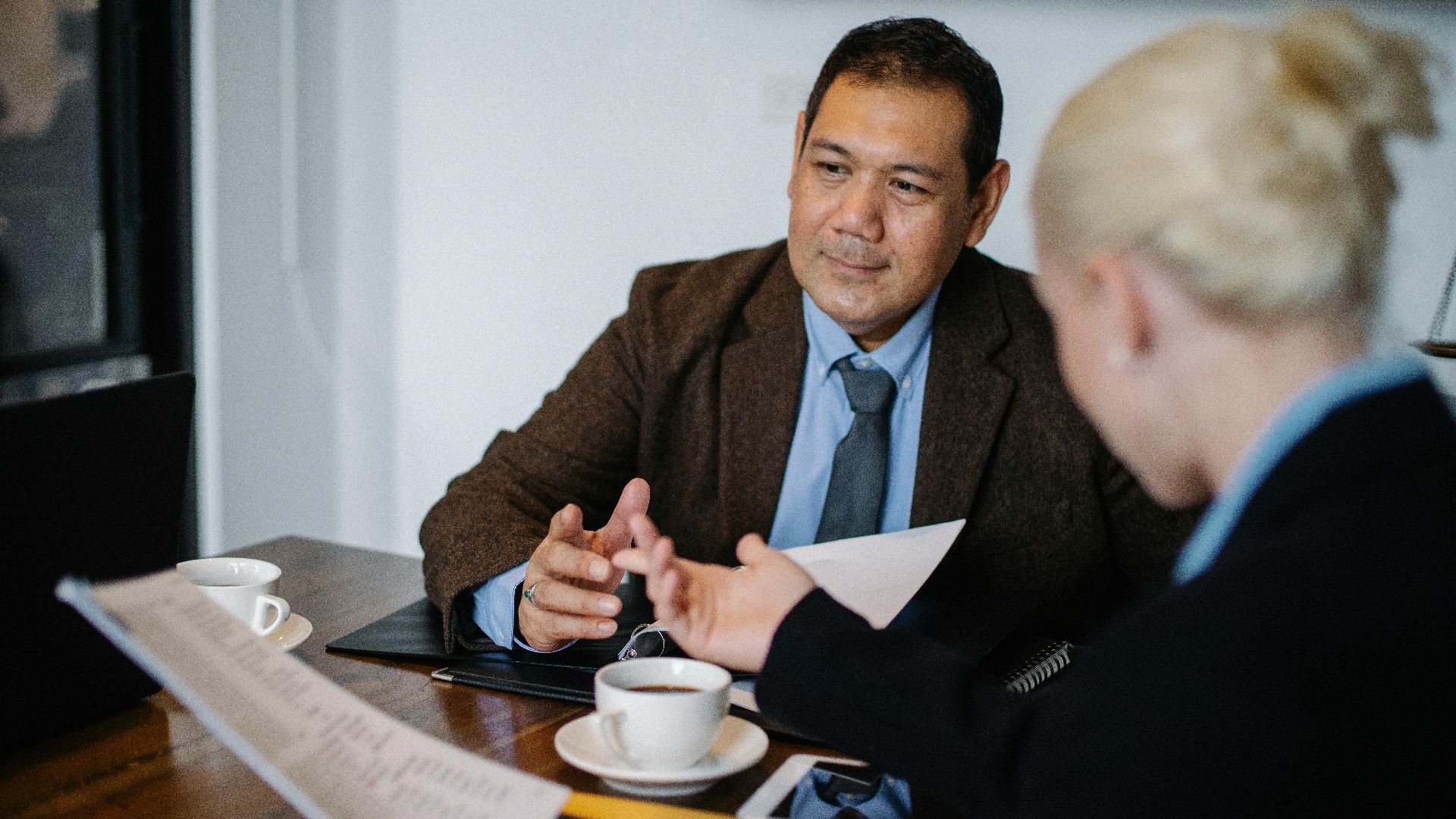 Professional diverse employees sitting at table with documents and cup of coffee and talking during work on new business project