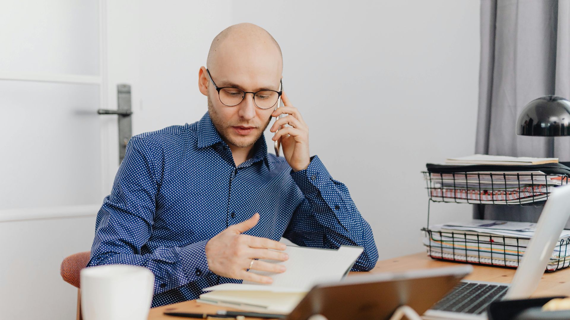 A bald professional man using a phone and making notes in an office environment.