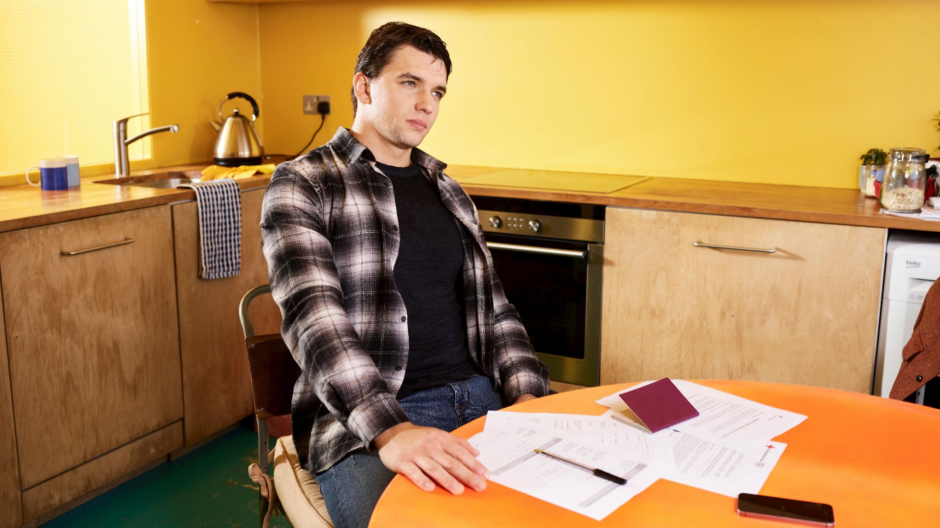 Man sitting at a kitchen table with documents and a passport, contemplating.
