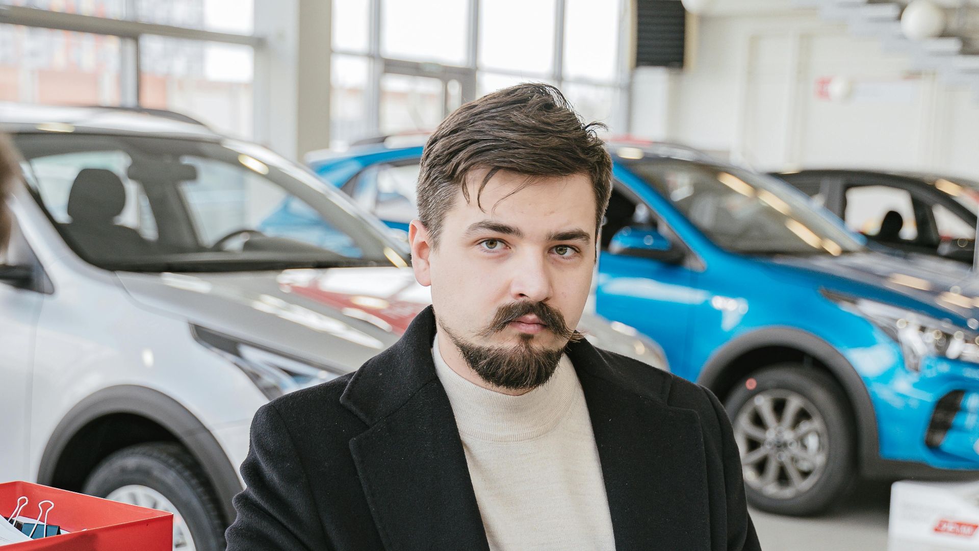 A man in a coat discusses with a sales representative in a bright, modern car showroom.