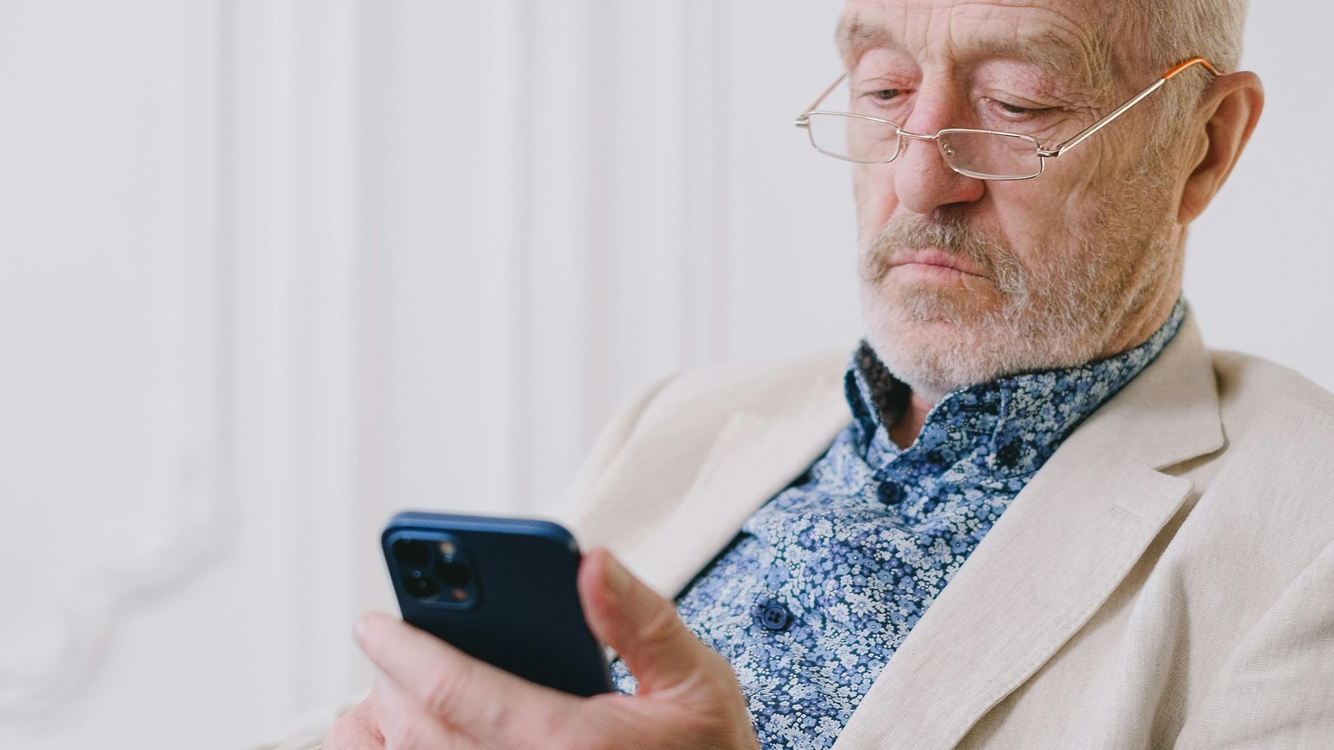 Elderly man using a smartphone with focus and ease while sitting indoors.