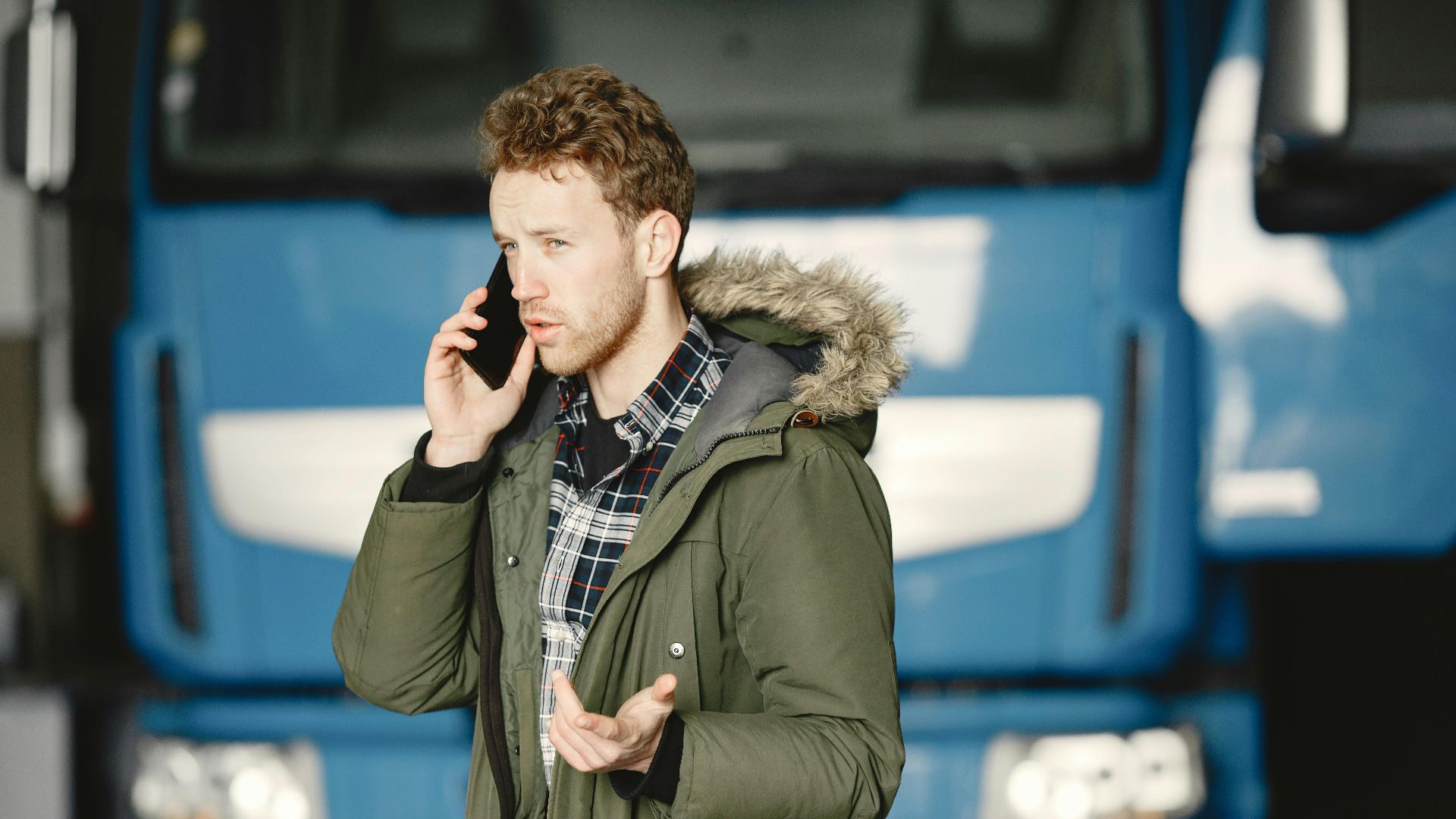 Man in a green parka talking on the phone in front of a blue truck.