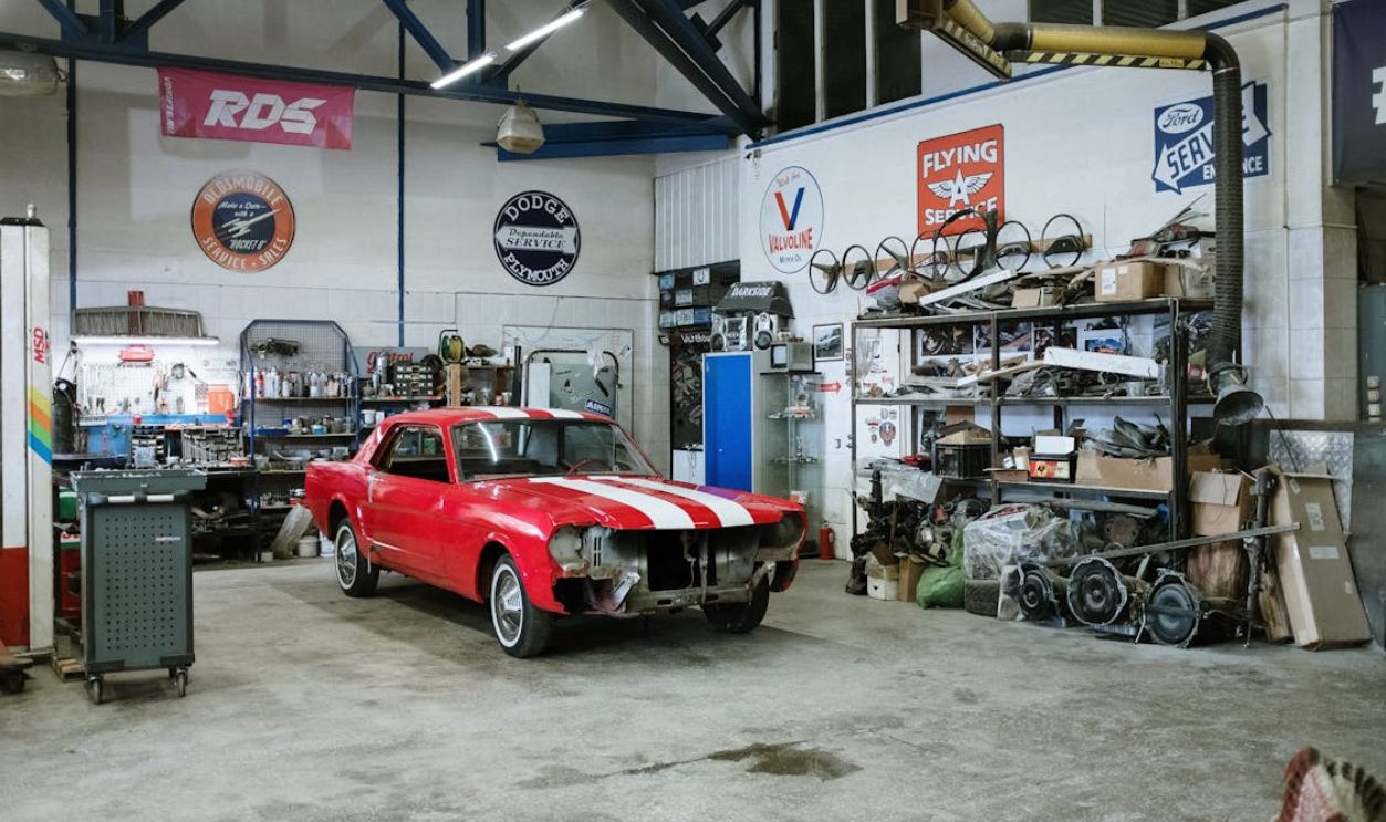 A vintage red car undergoing restoration in a well-equipped workshop with various tools and auto parts.