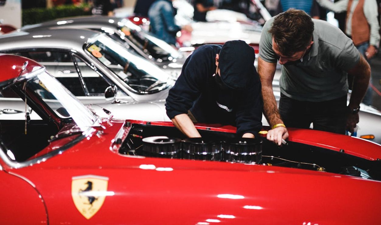 Red Ferrari with mechanics inspecting engine at a classic car show.
