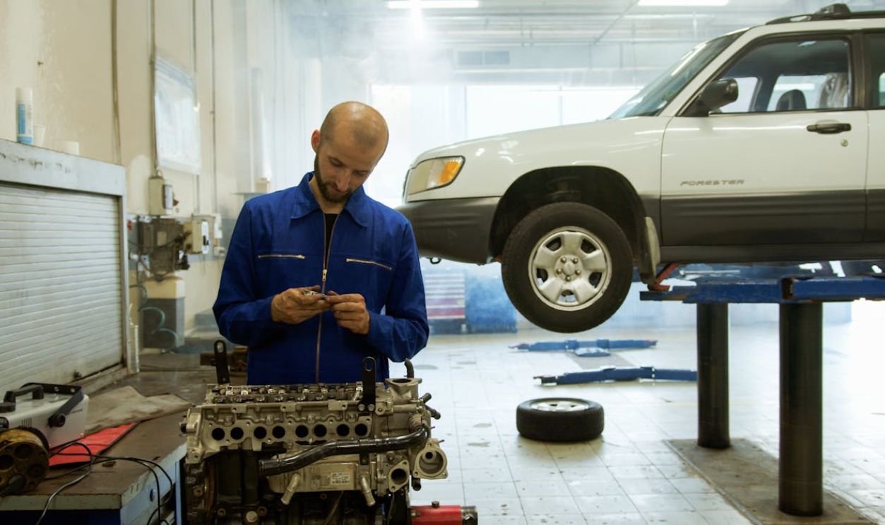A mechanic in blue uniform inspecting an engine in a professional auto repair workshop.