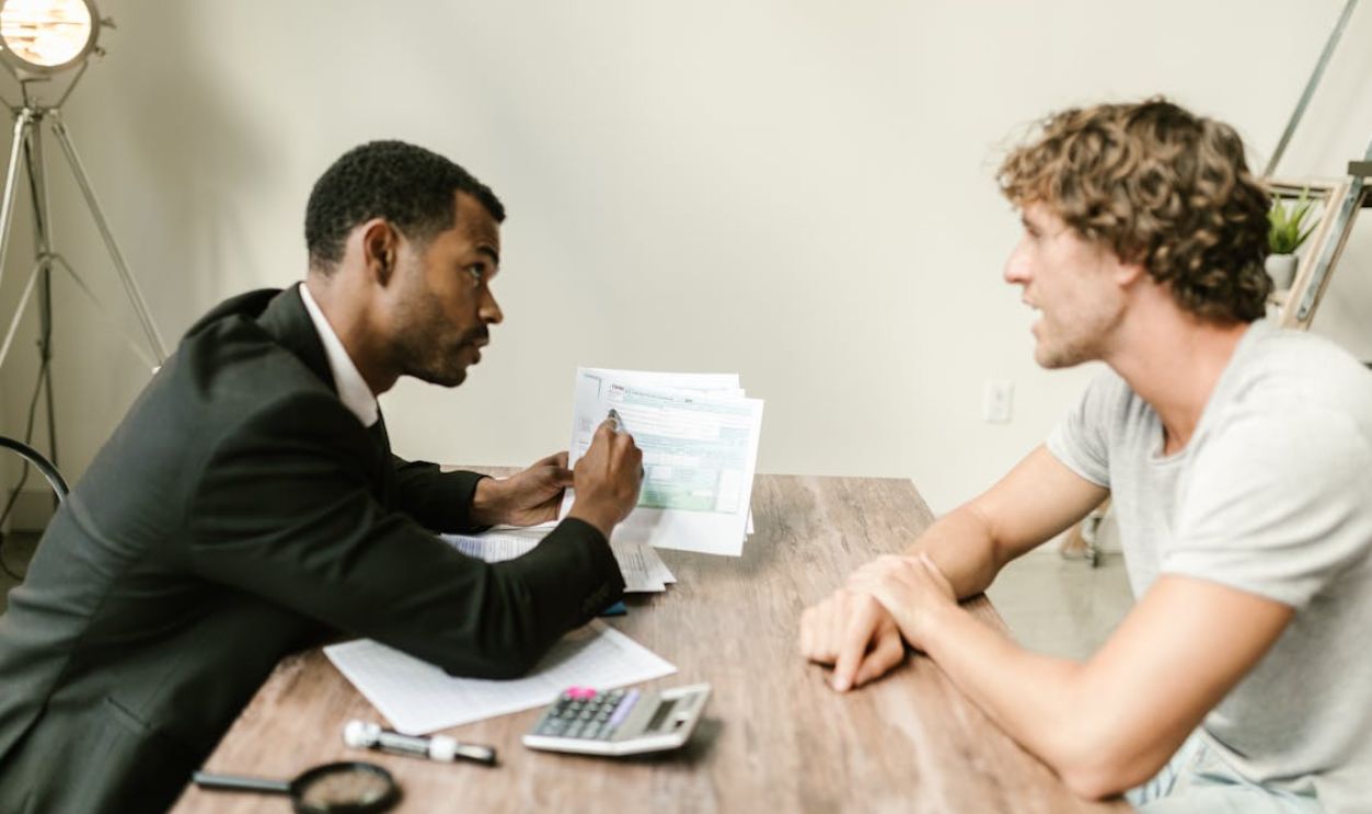 A financial advisor discusses paperwork with a client at a desk in a modern office.