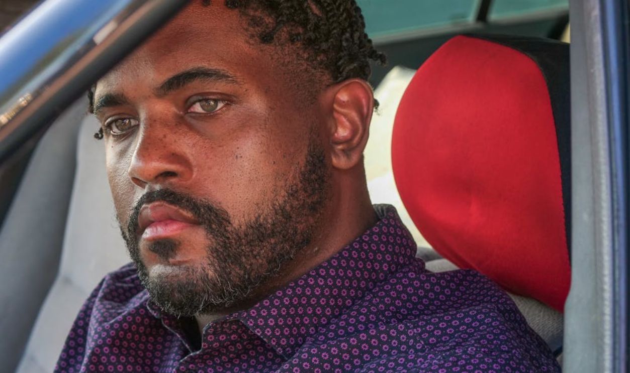 Close-up portrait of a man with facial hair sitting in a car staring intently
