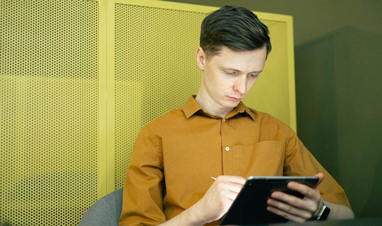 Young man in yellow shirt focused on using a tablet indoors, showcasing modern technology and study