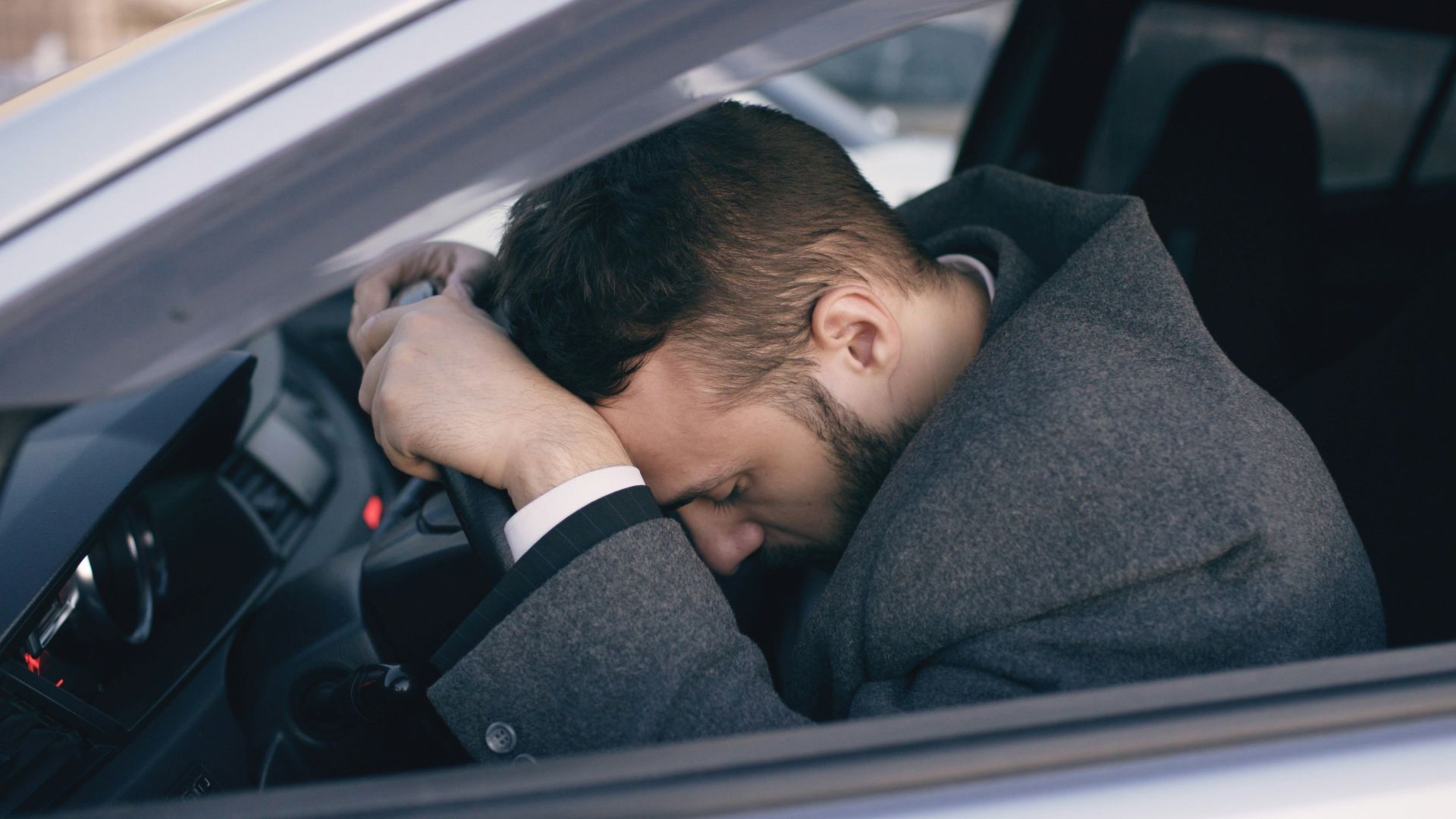 Man resting head on steering wheel in car.
