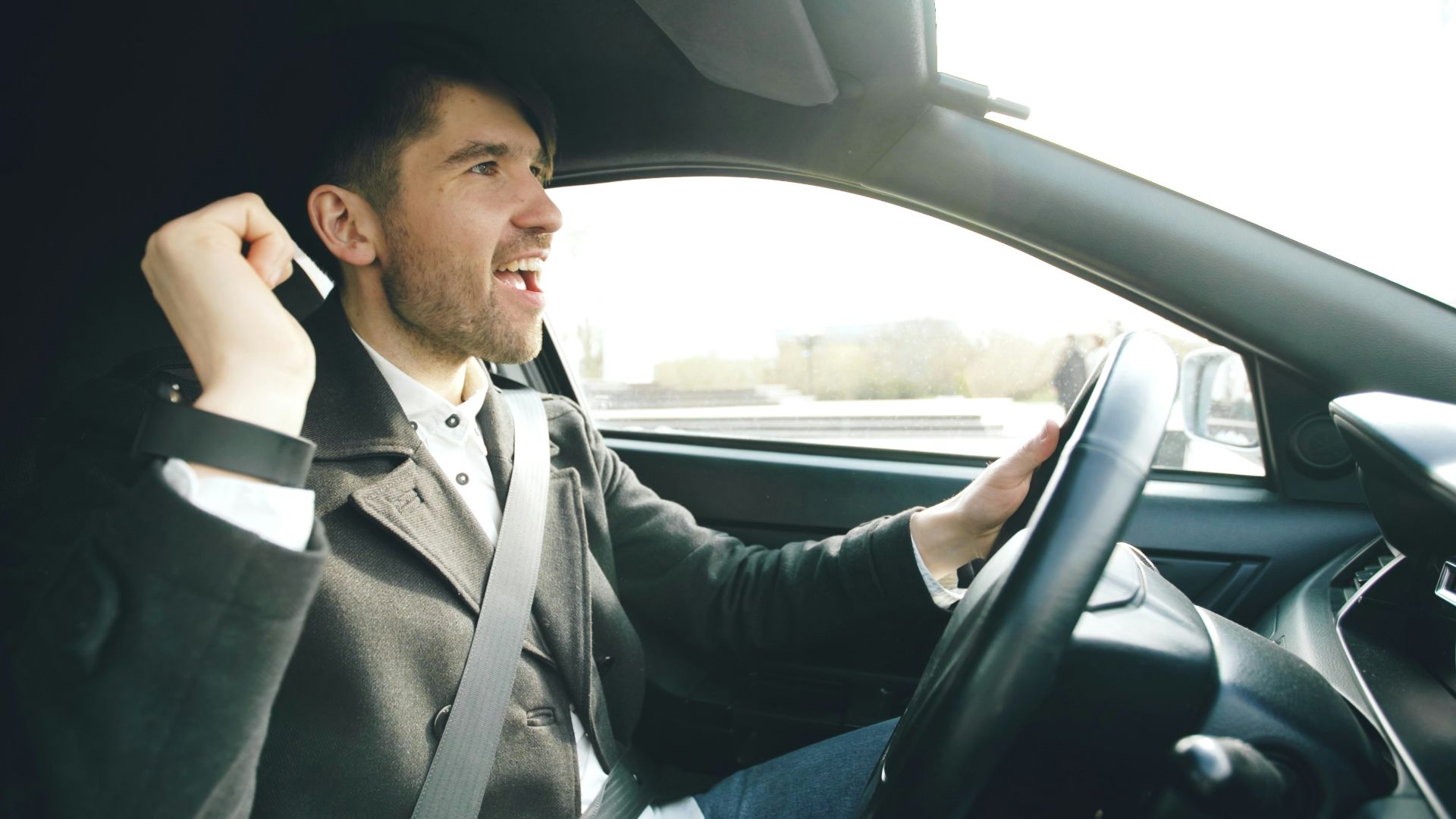 Man singing and driving a car enthusiastically.