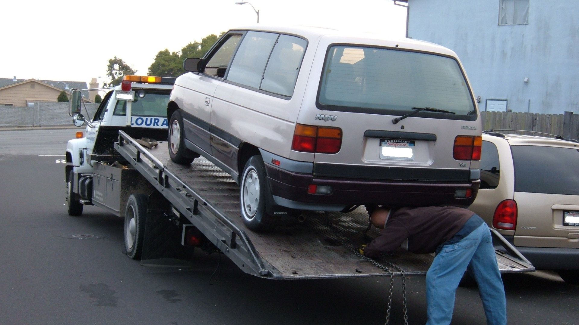 A Mazda MPV minivan being donated to a charitable organization is secured by chain onto the flatbed of a tow tuck.