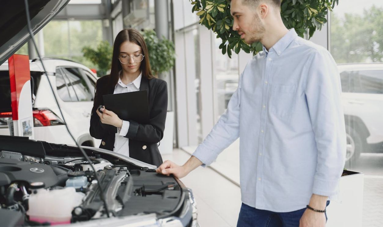 Man and woman examining car engine in dealership service area, focused on vehicle maintenance and functionality