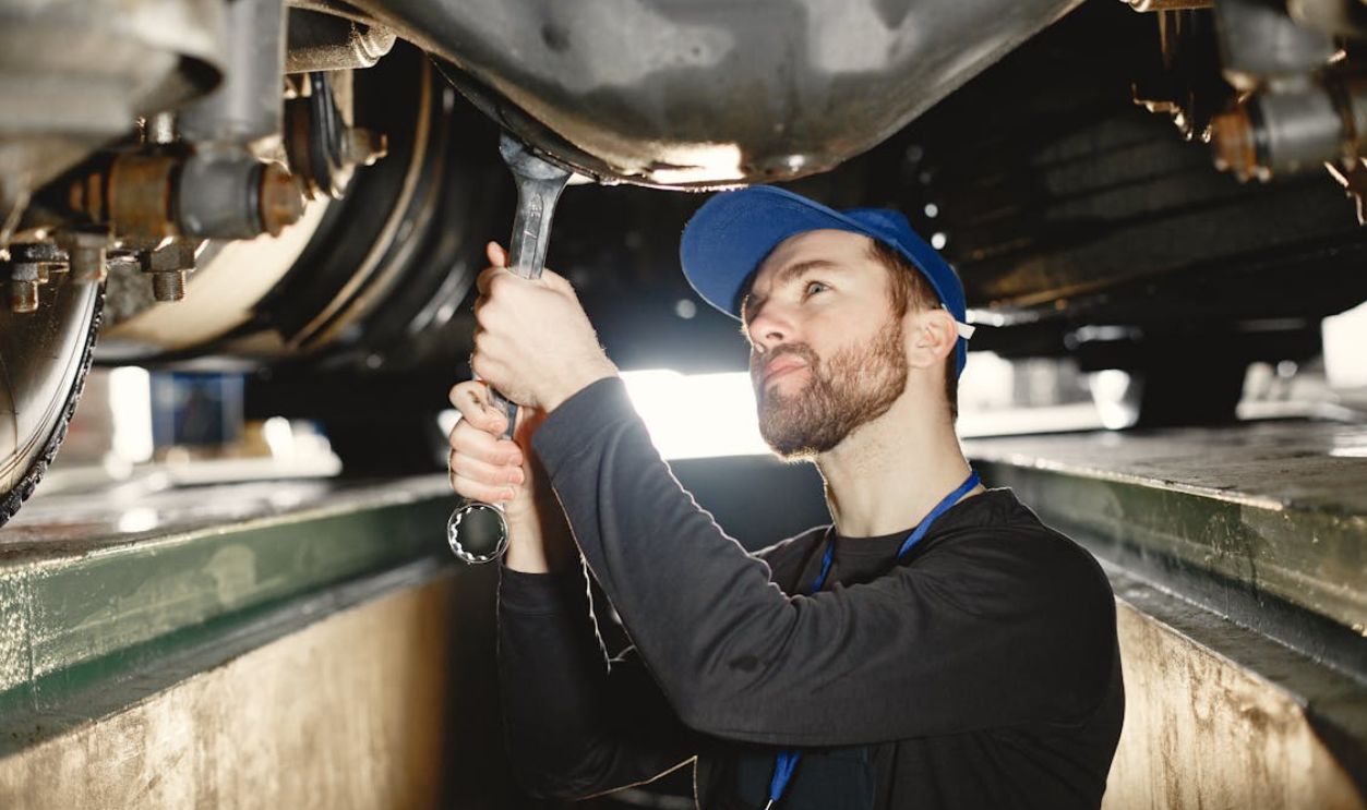 Auto mechanic repairing undercarriage in workshop with focused expression