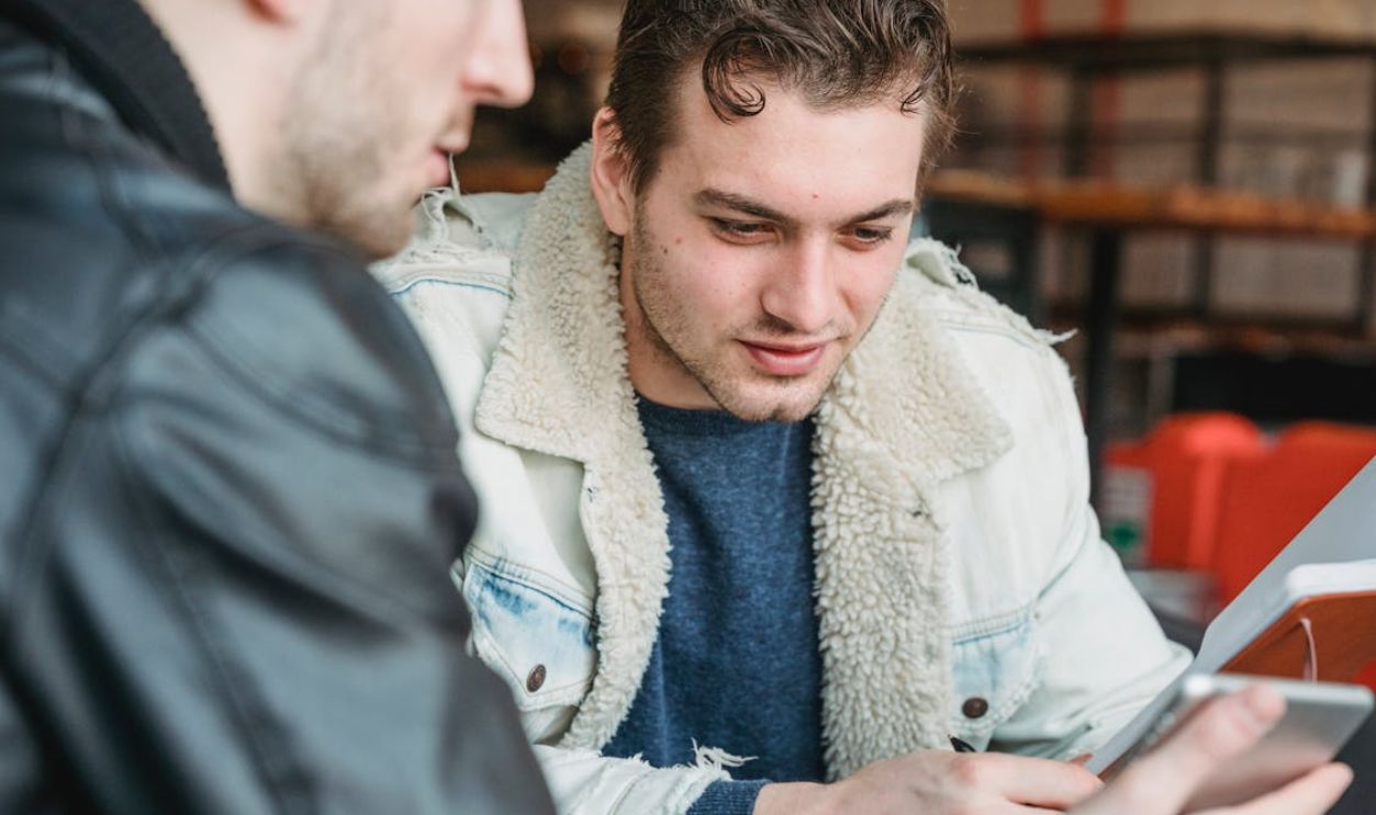 Two young men engaged in a discussion using a digital tablet in a cozy café environment