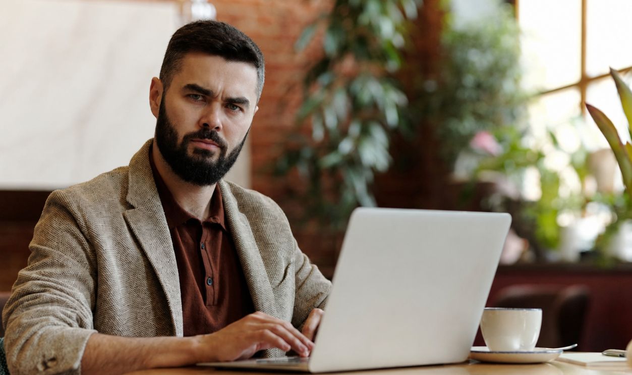 Businessman working on laptop in a cafe setting, surrounded by plants, sipping coffee