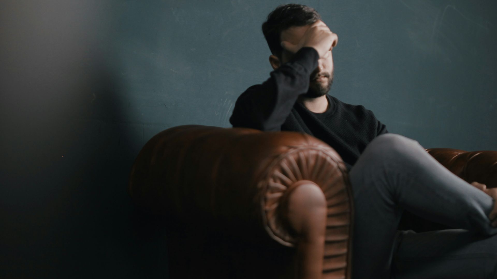 a man holds his head while sitting on a sofa