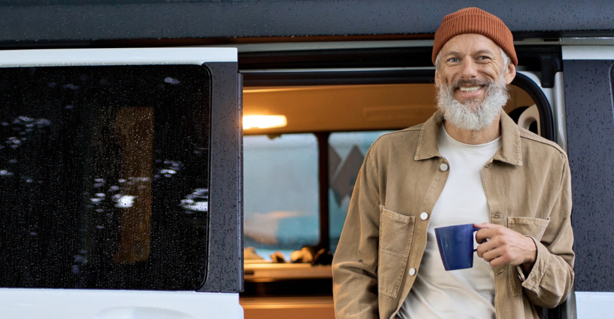 Happy older senior hipster man standing near rv camper van on vacation