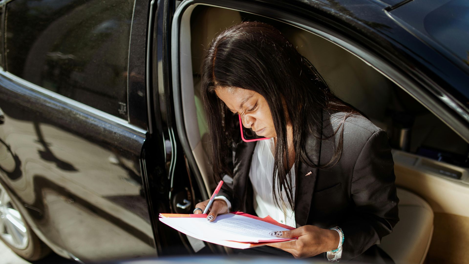 A focused businesswoman analyzes documents while sitting in her car.