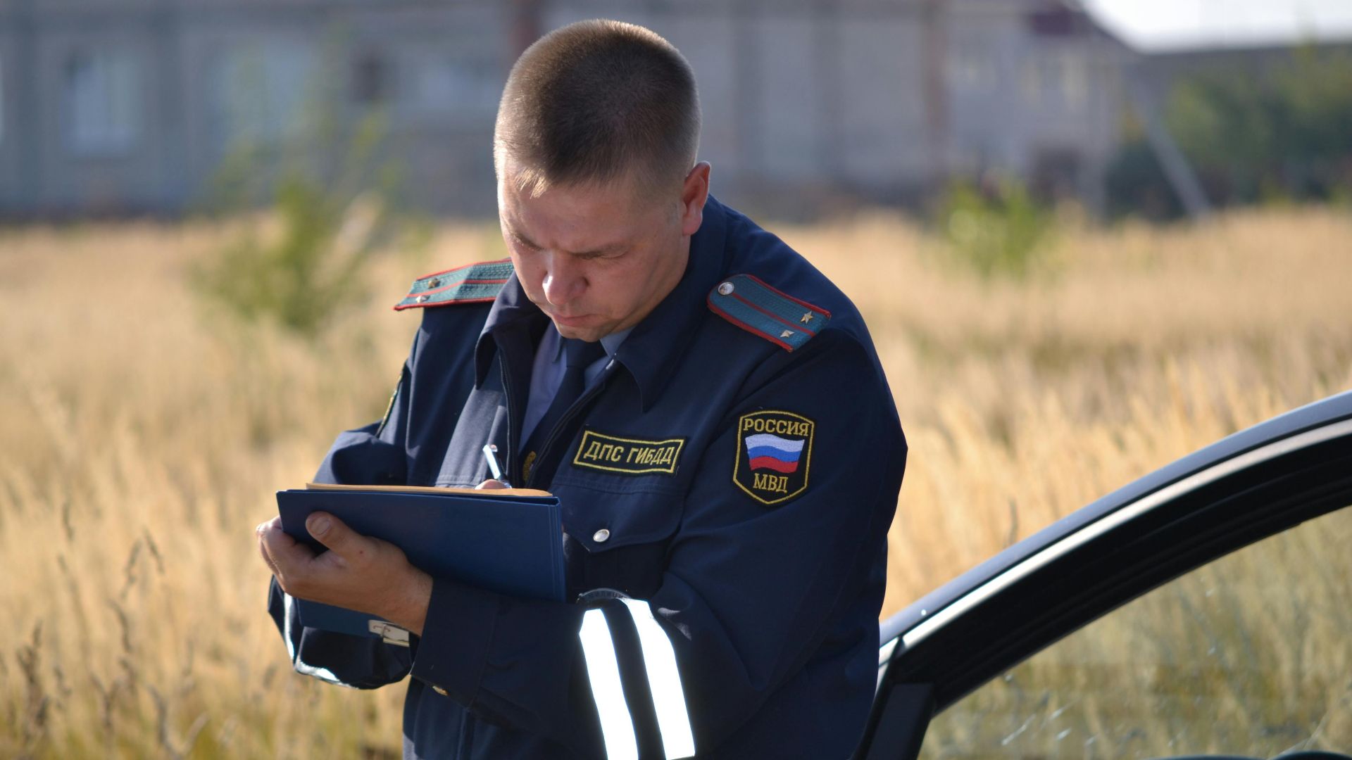 Police officer in uniform taking notes beside a car in a field.
