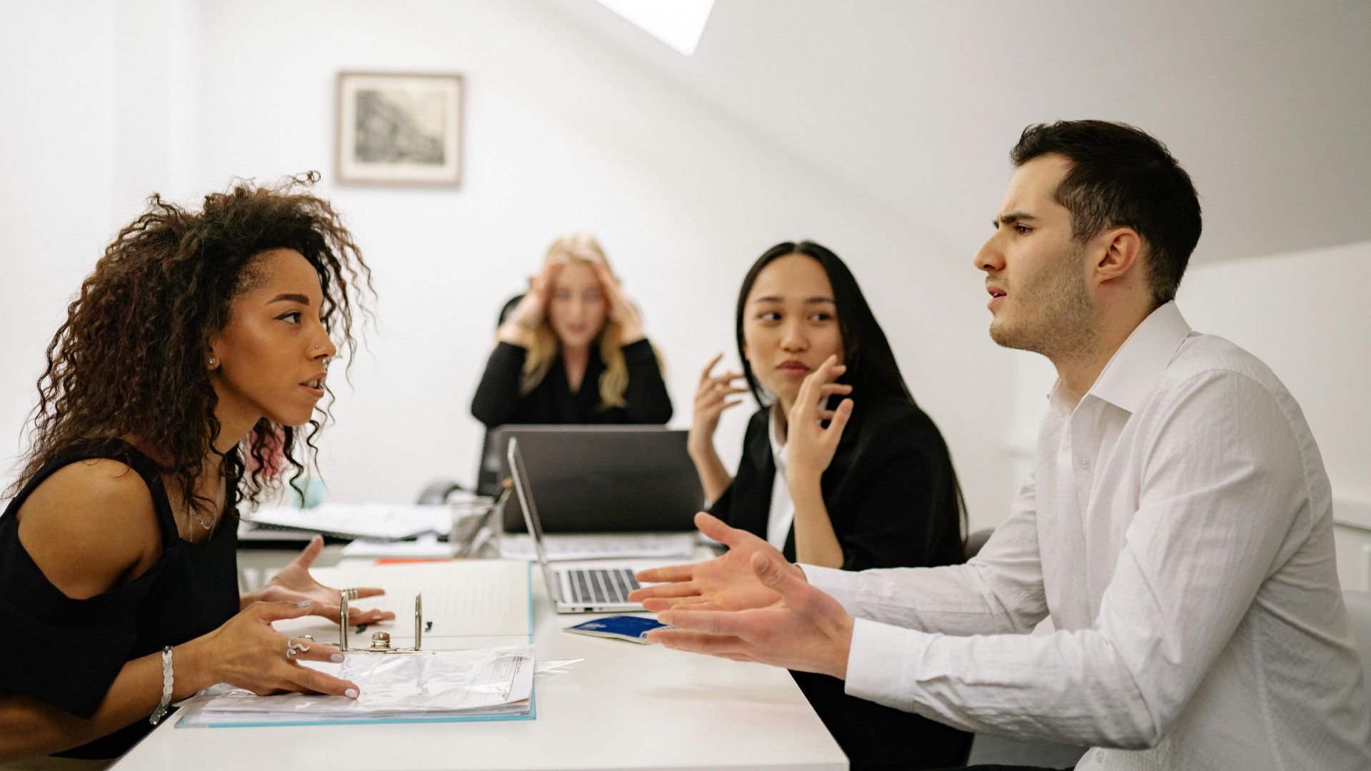 A multi-ethnic team engaged in a heated office discussion, displaying various emotions.