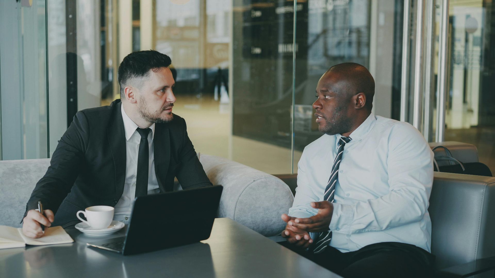Two businessmen discussing at a cafe with a laptop and coffee.