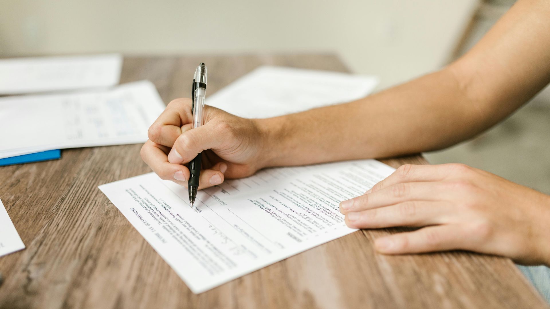 Hand filling out paperwork with a pen, showcasing focus on document completion.