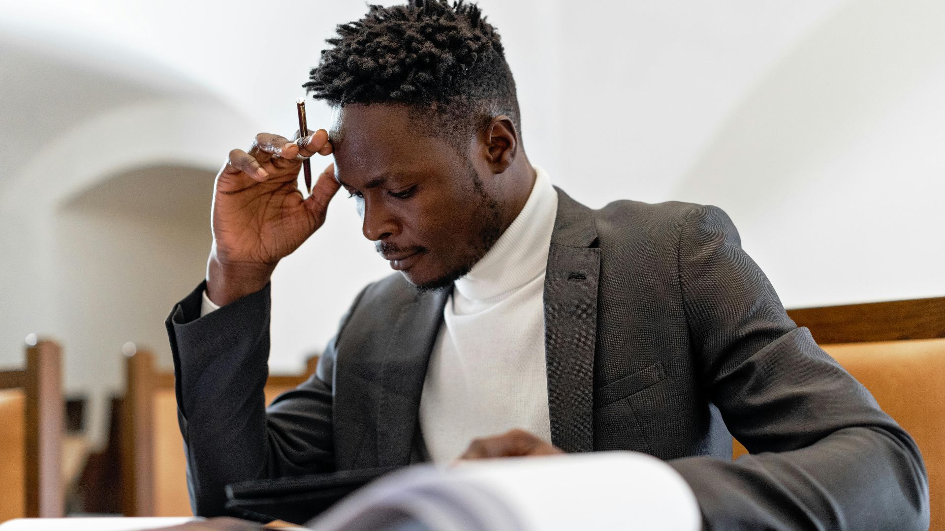 A focused businessman in a suit examines documents while deep in thought in an office setting.