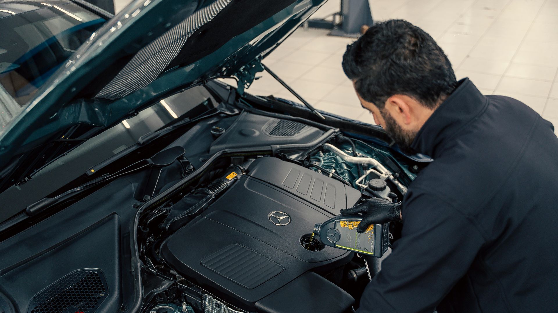 Mechanic inspecting and filling engine oil in a car at an indoor service center.