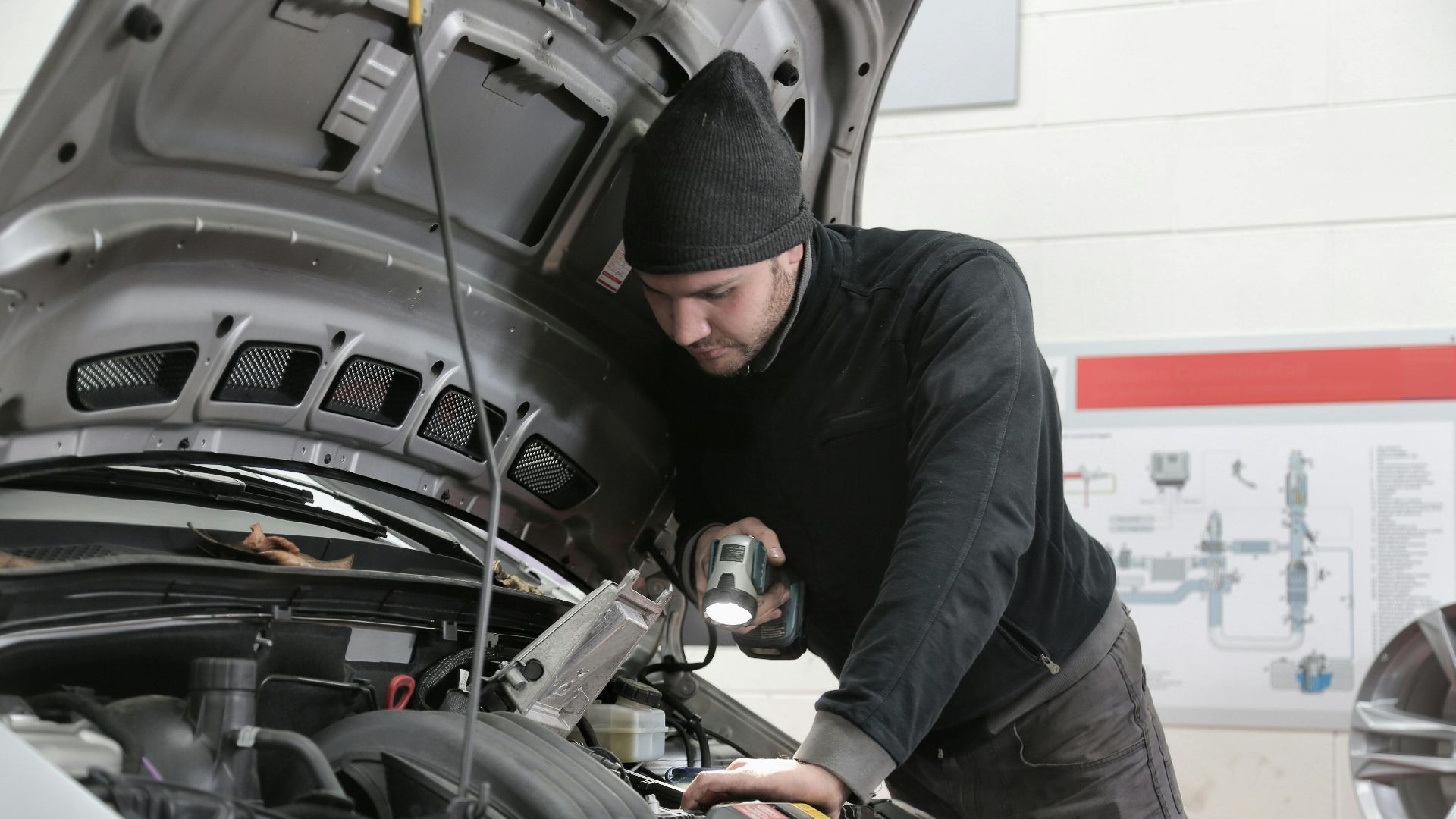 A mechanic closely inspects a car engine in a garage using a flashlight, ensuring proper maintenance.