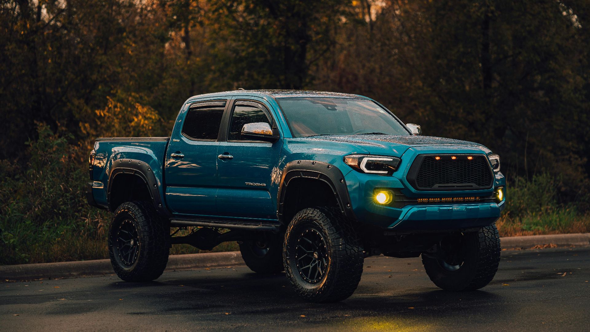 A lifted blue pickup truck parked on a wet road in a wooded environment.