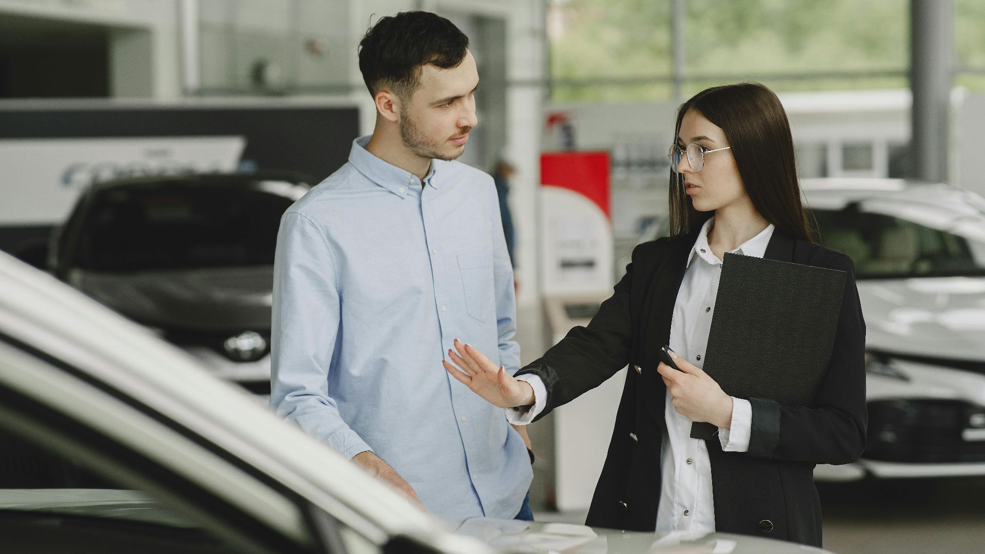 A salesperson and customer discussing car features in a dealership setting.