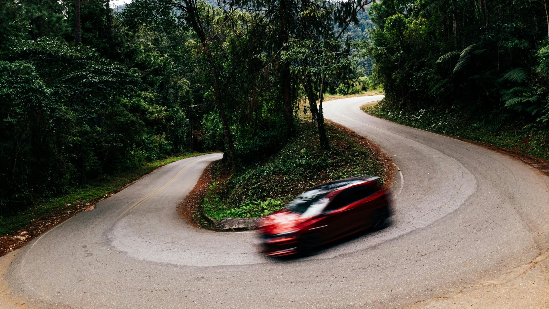Long exposure of modern luxury automobile driving fast in motion on asphalt road bend near green trees