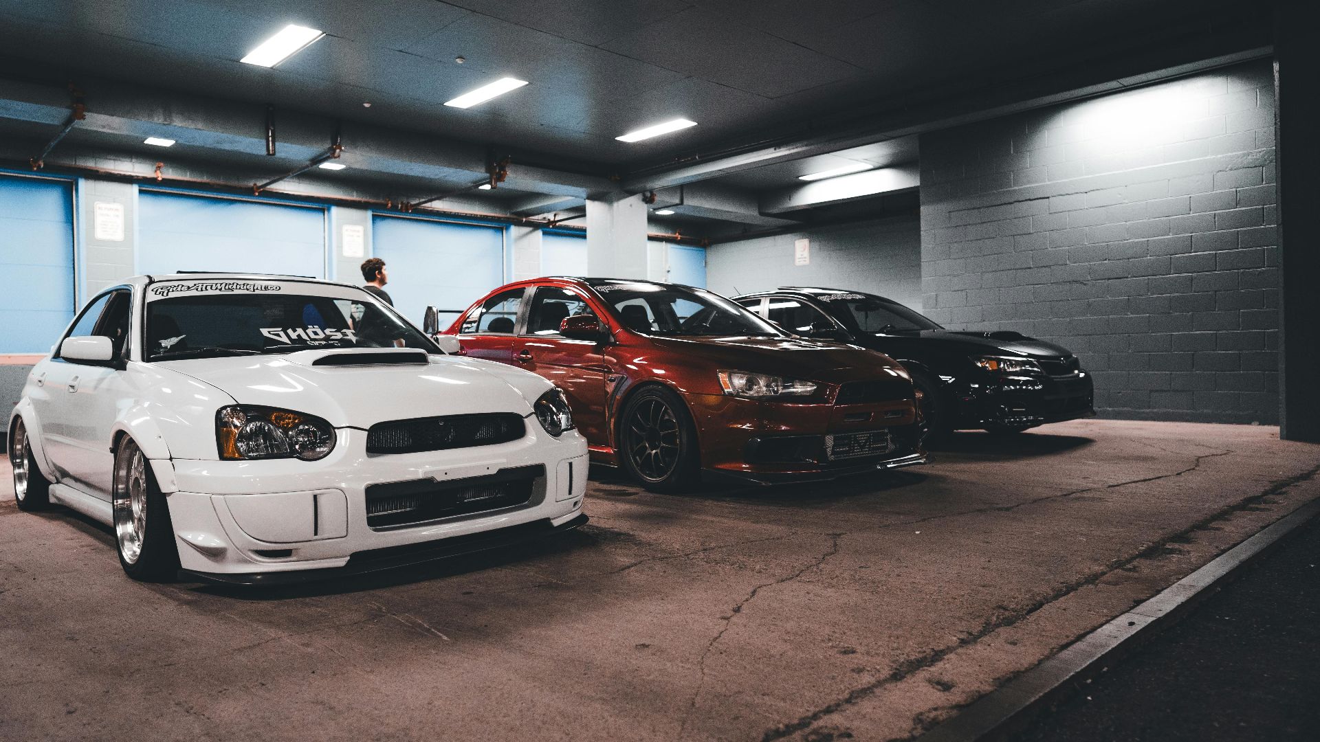 A trio of modified sports cars parked inside a dimly lit underground garage.